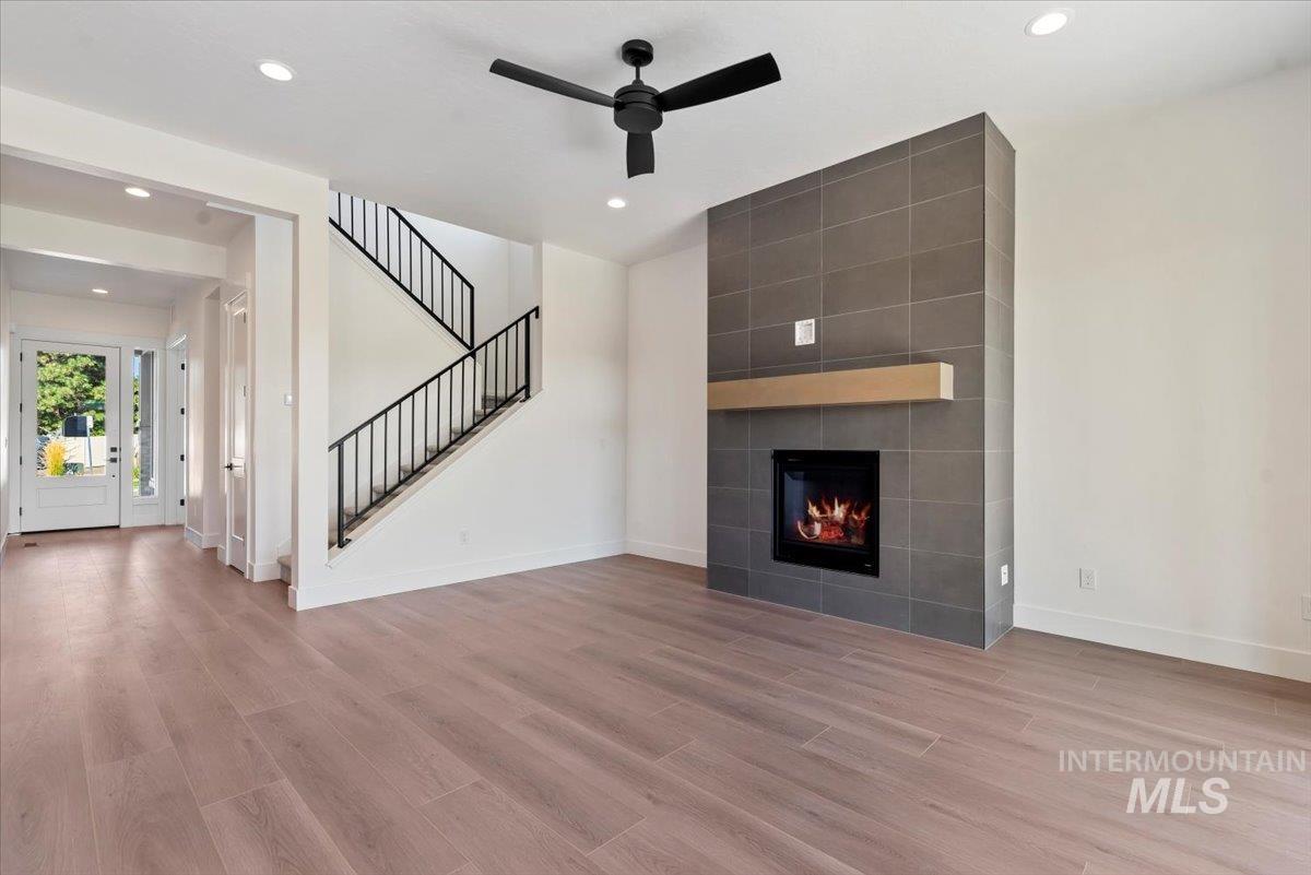 Unfurnished living room featuring light wood-type flooring, recessed lighting, ceiling fan, a fireplace, and stairs