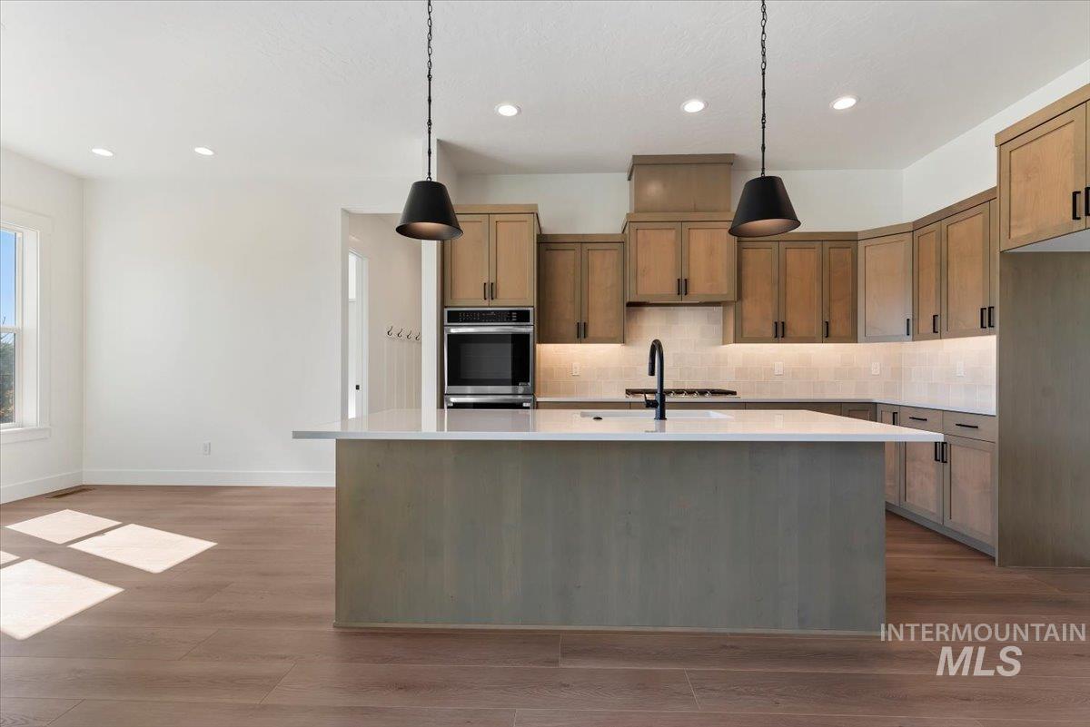 Kitchen featuring decorative light fixtures, tasteful backsplash, brown cabinetry, a kitchen island with sink, and recessed lighting