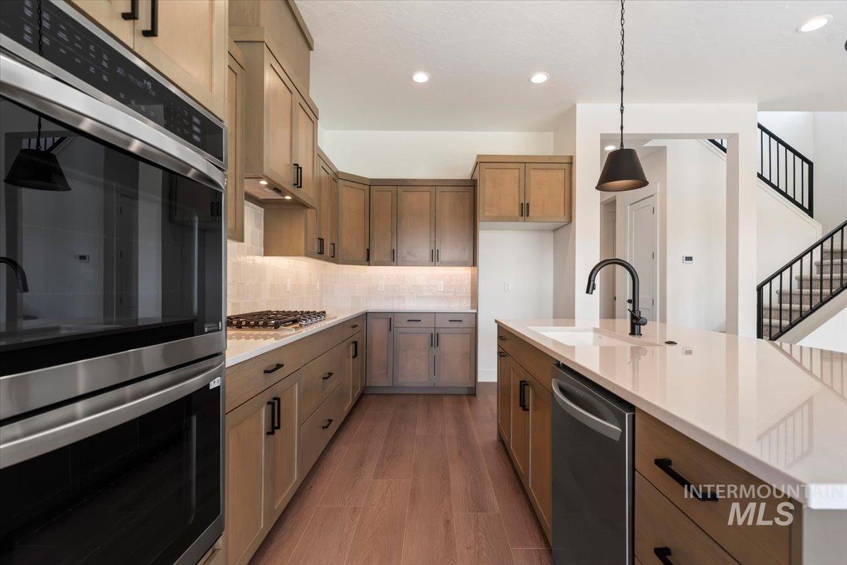 Kitchen featuring appliances with stainless steel finishes, an island with sink, tasteful backsplash, light wood-type flooring, and decorative light fixtures