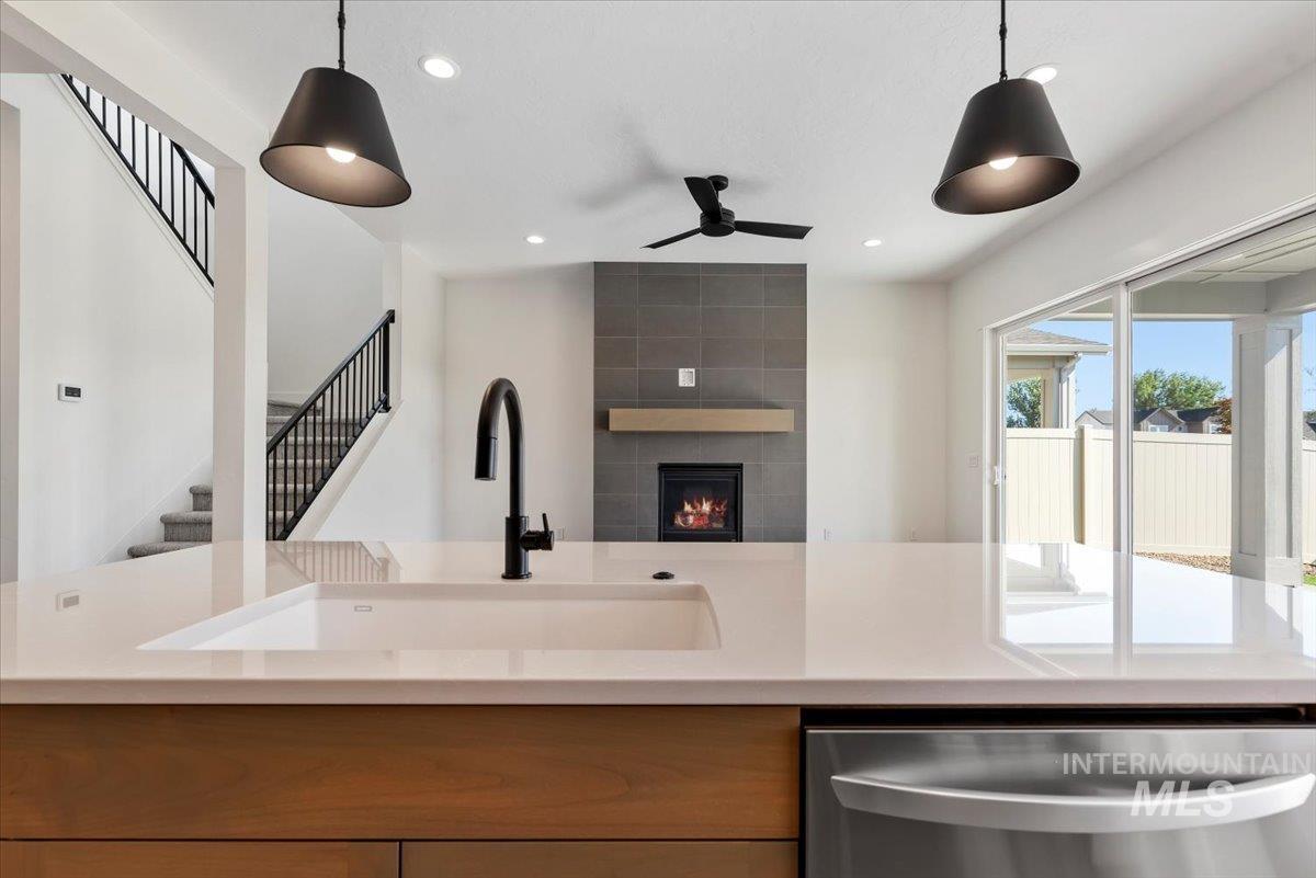 Kitchen featuring dishwasher, a fireplace, light stone counters, decorative light fixtures, and open floor plan