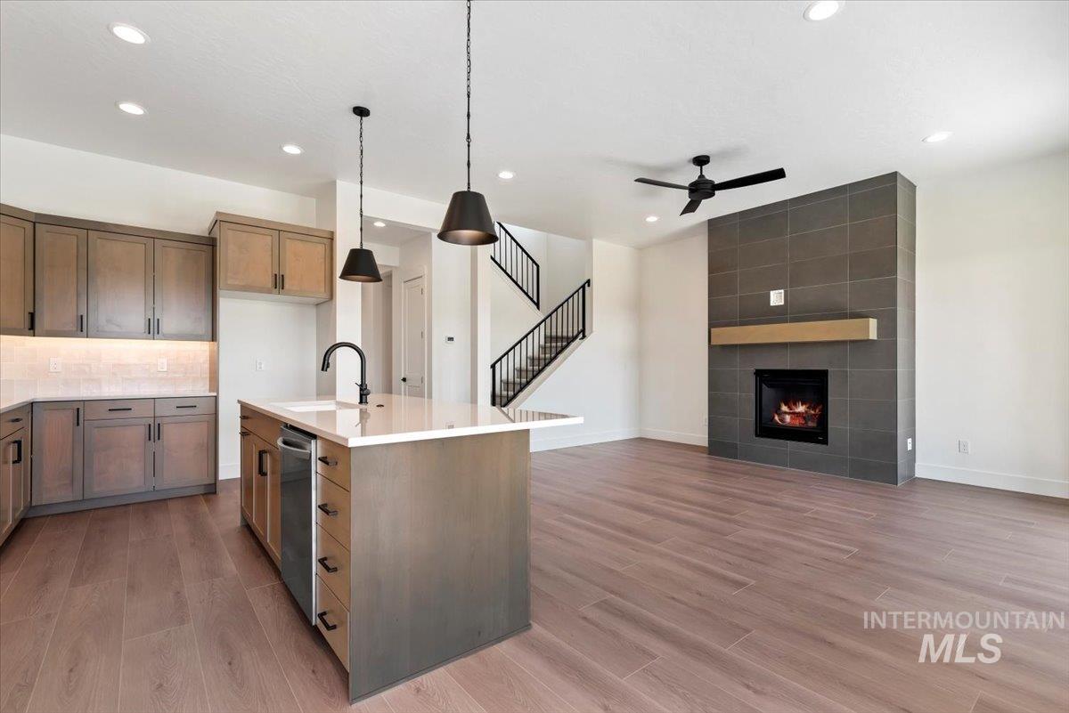 Kitchen with hanging light fixtures, a ceiling fan, light stone countertops, a tile fireplace, and open floor plan