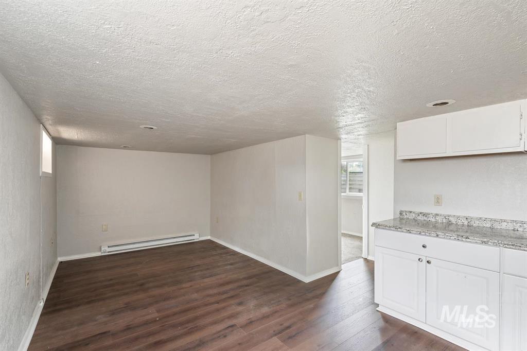 Unfurnished living room featuring dark wood finished floors, a baseboard heating unit, and a textured ceiling