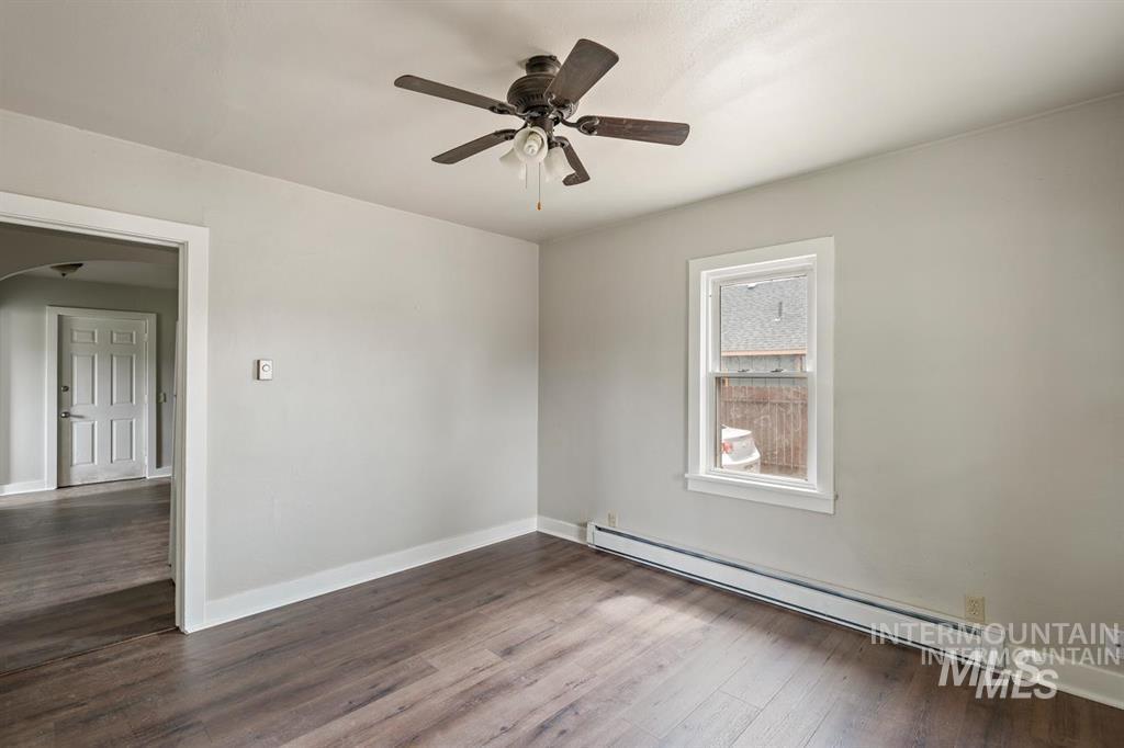 Unfurnished room with a baseboard heating unit, dark wood-style flooring, arched walkways, and a ceiling fan