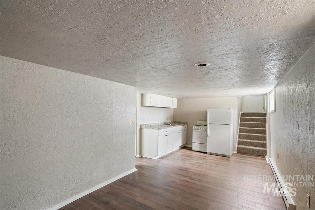 Unfurnished living room featuring a textured wall, a baseboard radiator, dark wood-type flooring, a textured ceiling, and stairs