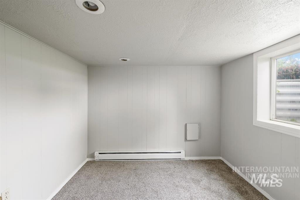 Empty room featuring carpet floors, a textured ceiling, and a baseboard radiator