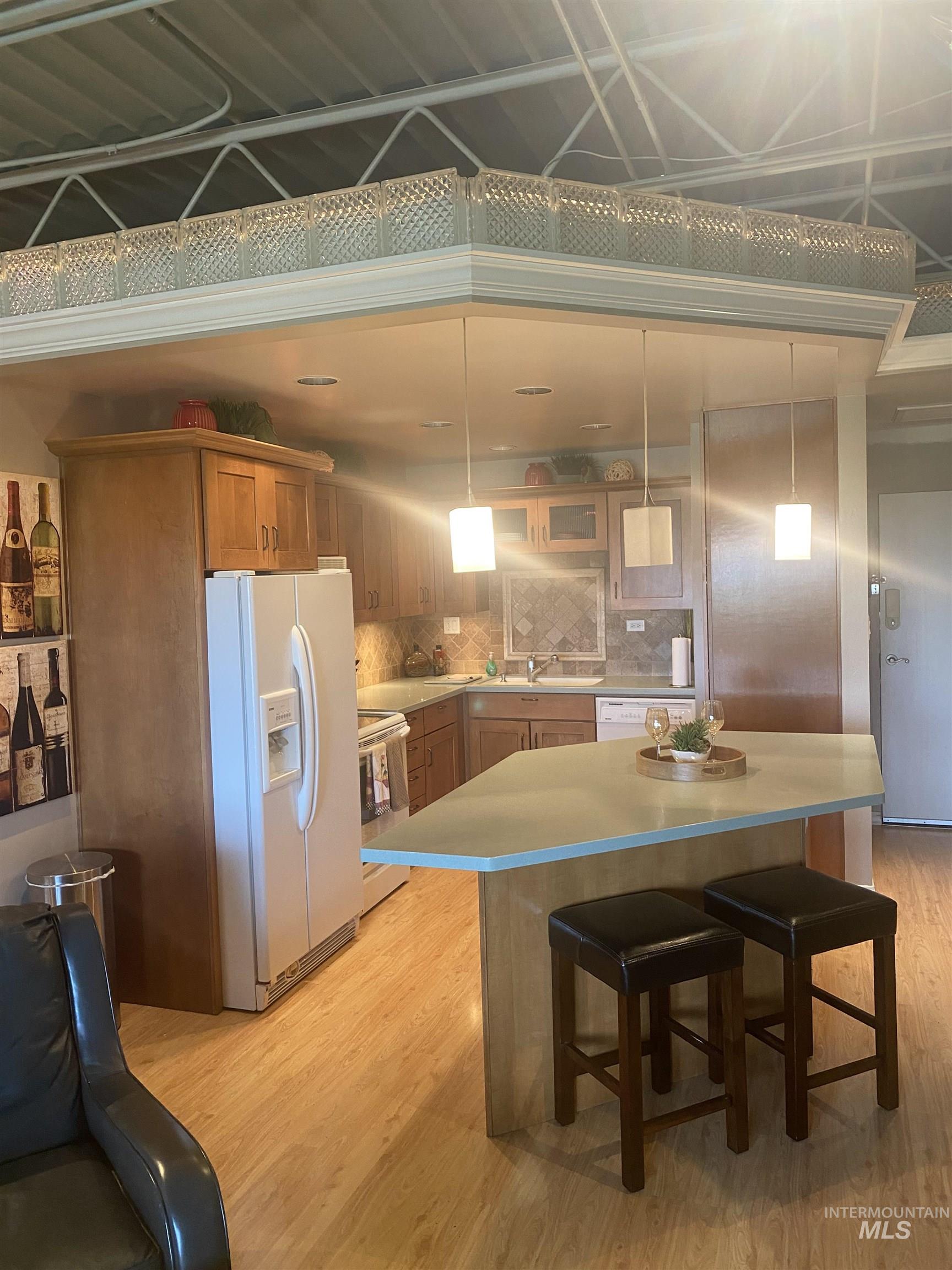 Kitchen with white appliances, hanging light fixtures, a breakfast bar, and light wood-style flooring