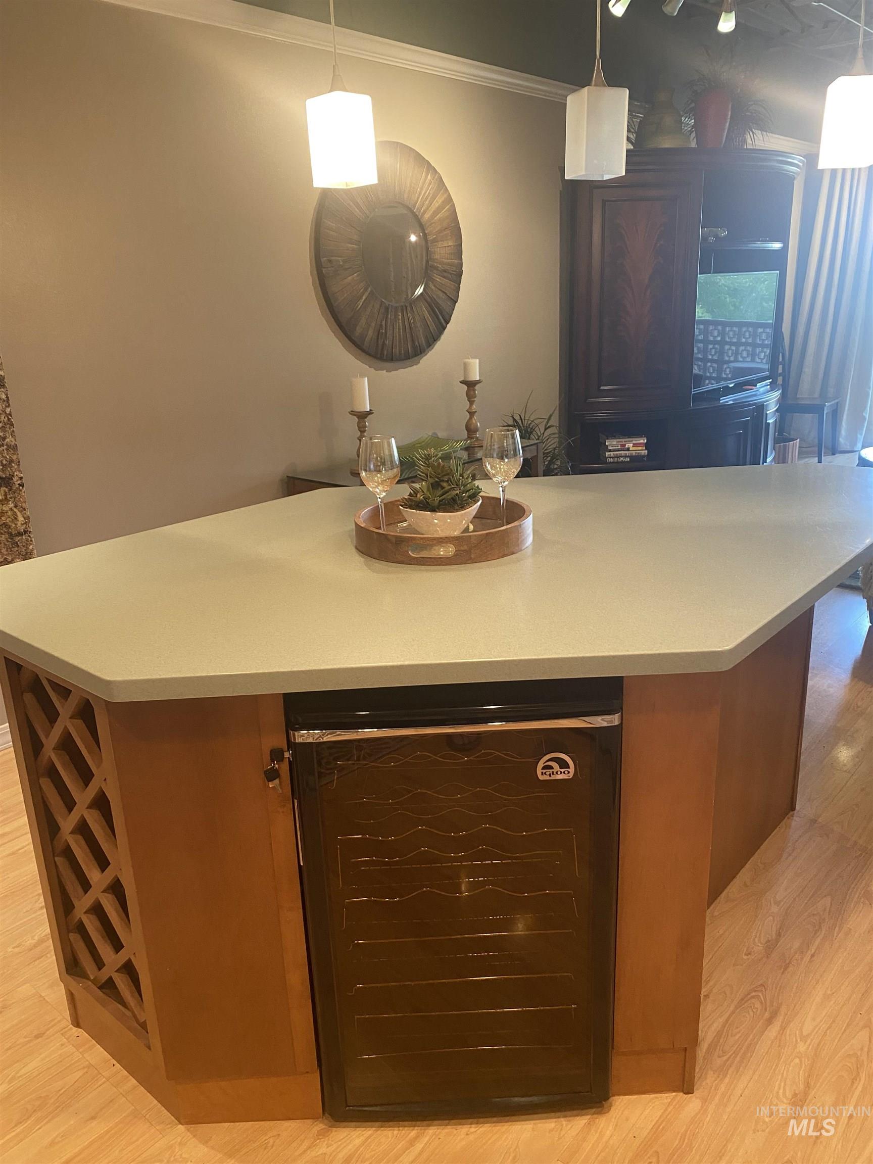 Kitchen with beverage cooler, a center island, light wood-style floors, decorative light fixtures, and crown molding