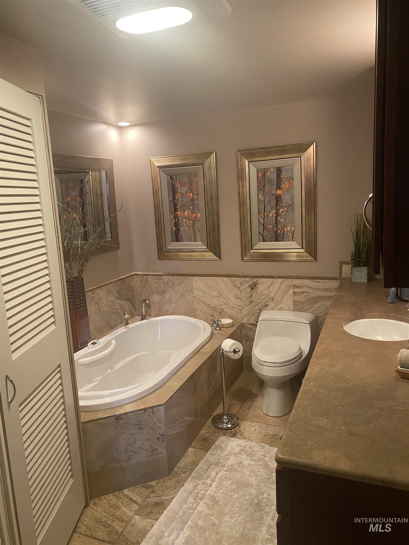 Bathroom with a garden tub, vanity, a closet, and tile walls