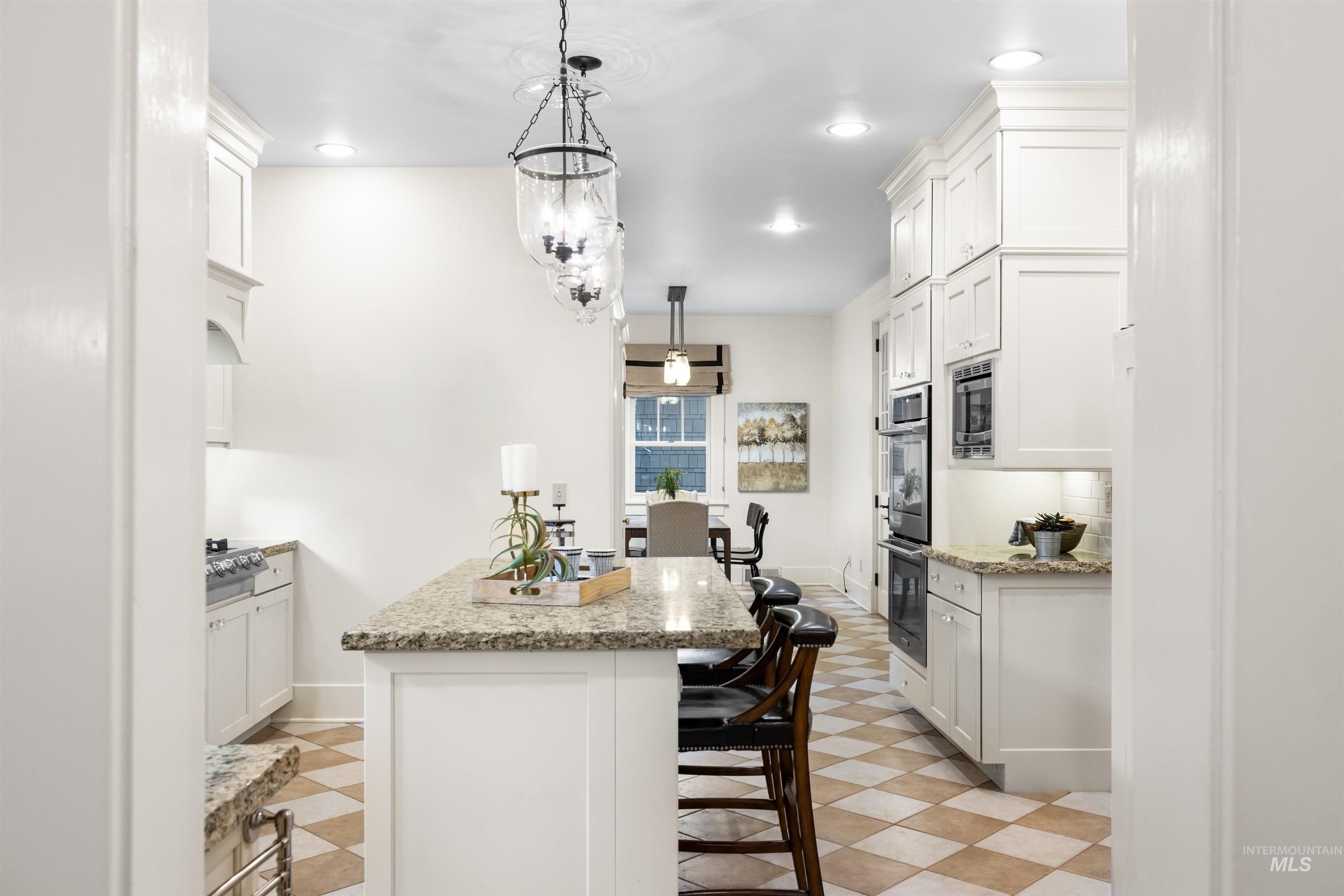 Kitchen featuring white cabinets, a breakfast bar, pendant lighting, light stone countertops, and recessed lighting