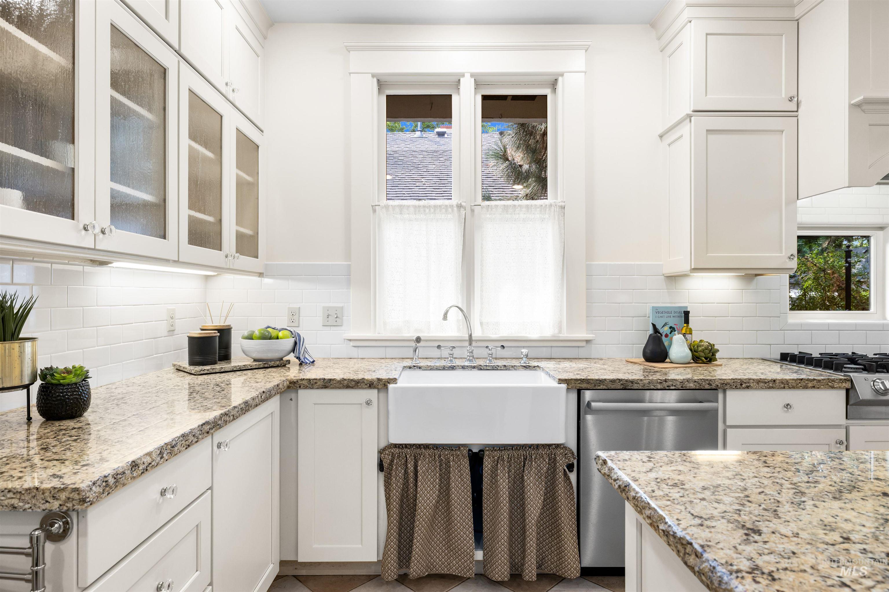 Kitchen with white cabinetry, appliances with stainless steel finishes, decorative backsplash, and light stone countertops