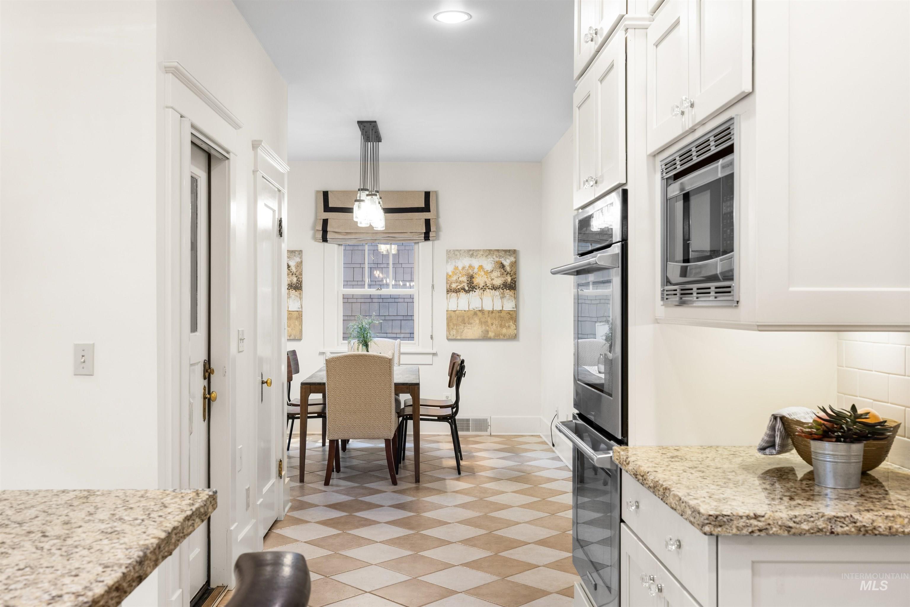 Kitchen with white cabinets, appliances with stainless steel finishes, light stone countertops, and decorative light fixtures