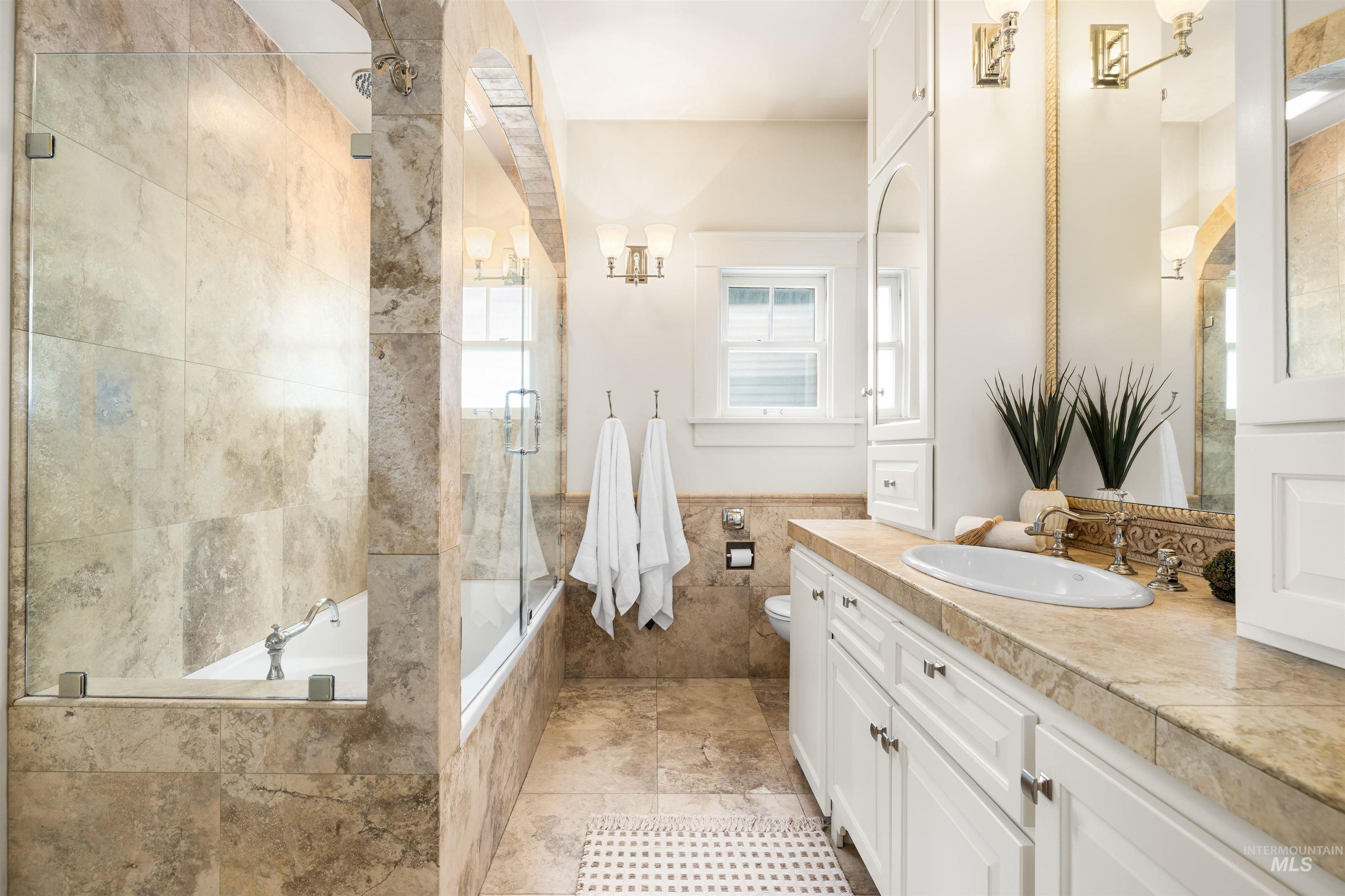 Bathroom with tiled shower / bath combo, vanity, tile walls, light tile patterned floors, and wainscoting