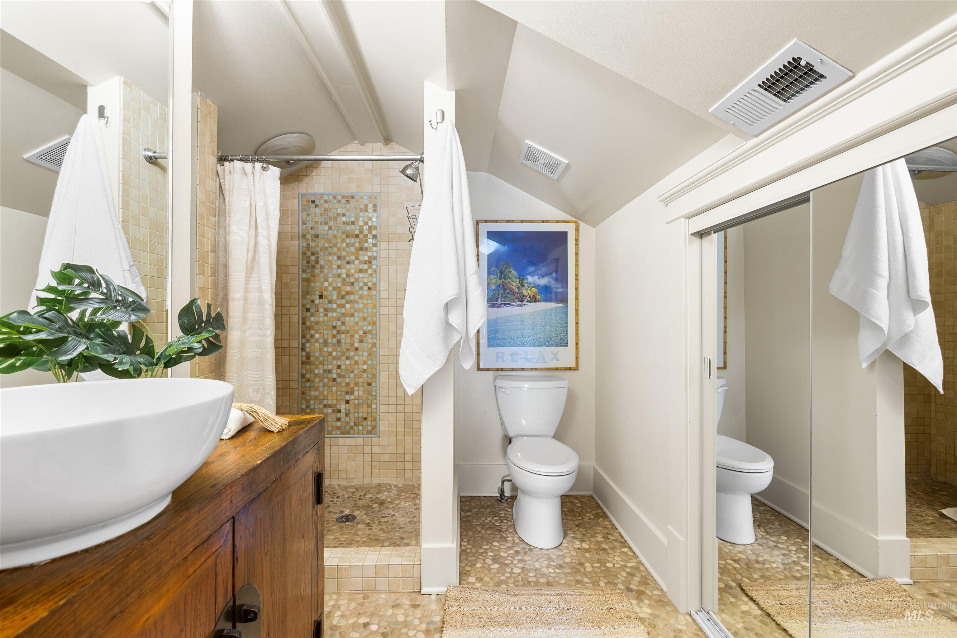 Full bath with walk in shower, vanity, vaulted ceiling, and light tile patterned floors
