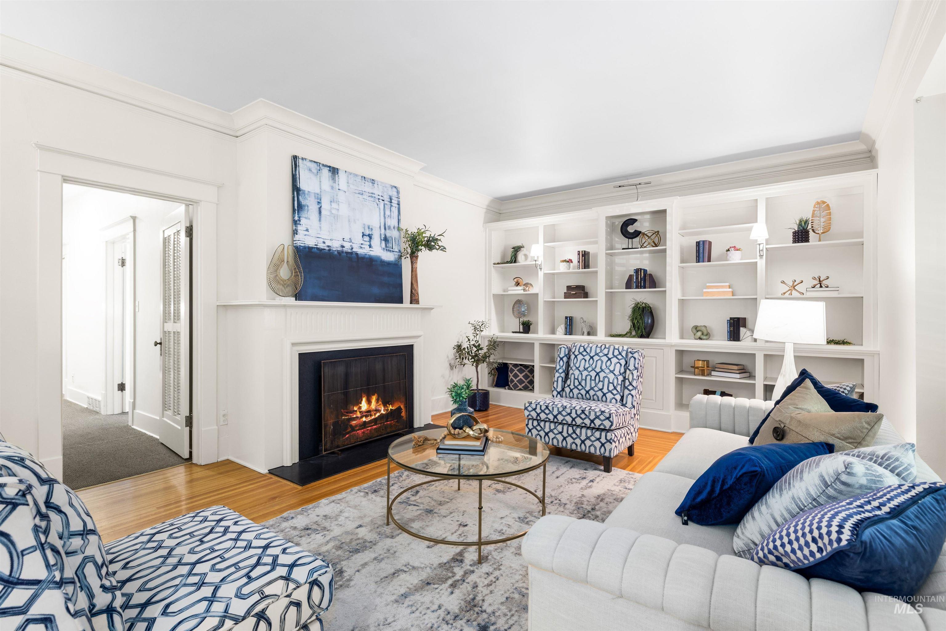 Living room featuring wood finished floors, crown molding, and a lit fireplace