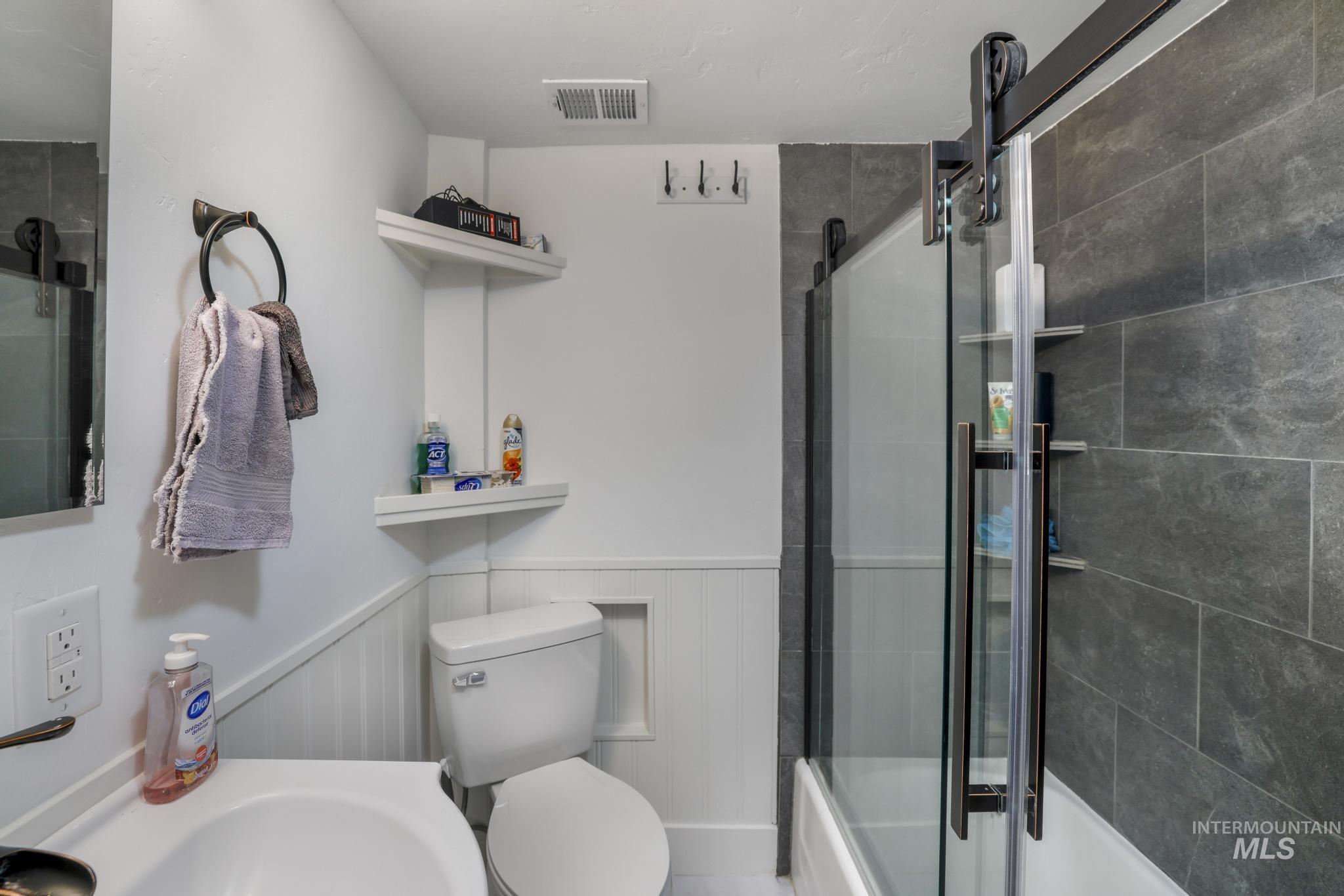 Full bath featuring enclosed tub / shower combo and wainscoting