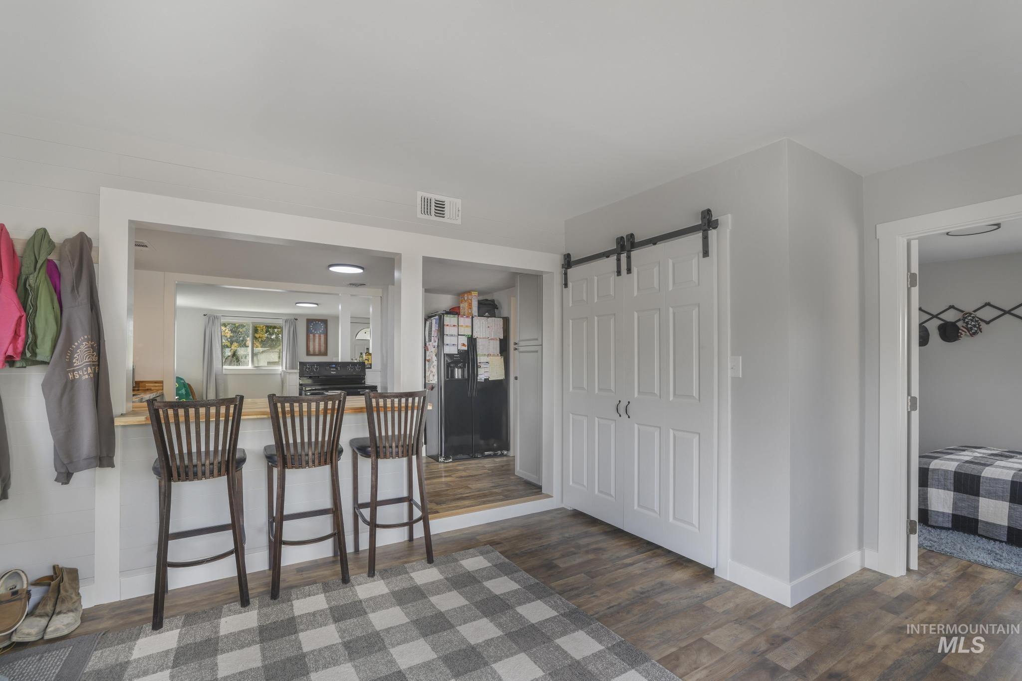 Kitchen with a barn door, black appliances, a breakfast bar area, dark wood finished floors, and light countertops
