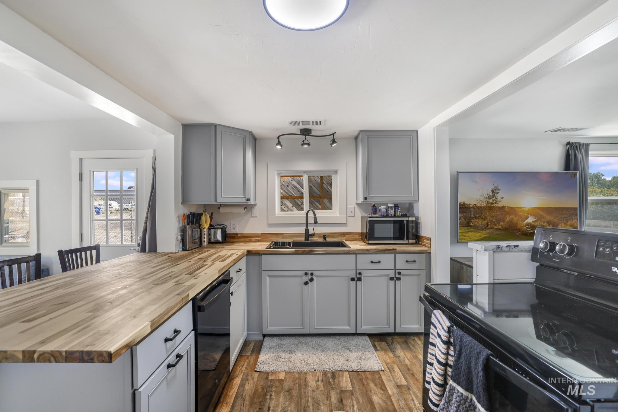 Kitchen featuring gray cabinetry, black appliances, wooden counters, dark wood finished floors, and a peninsula