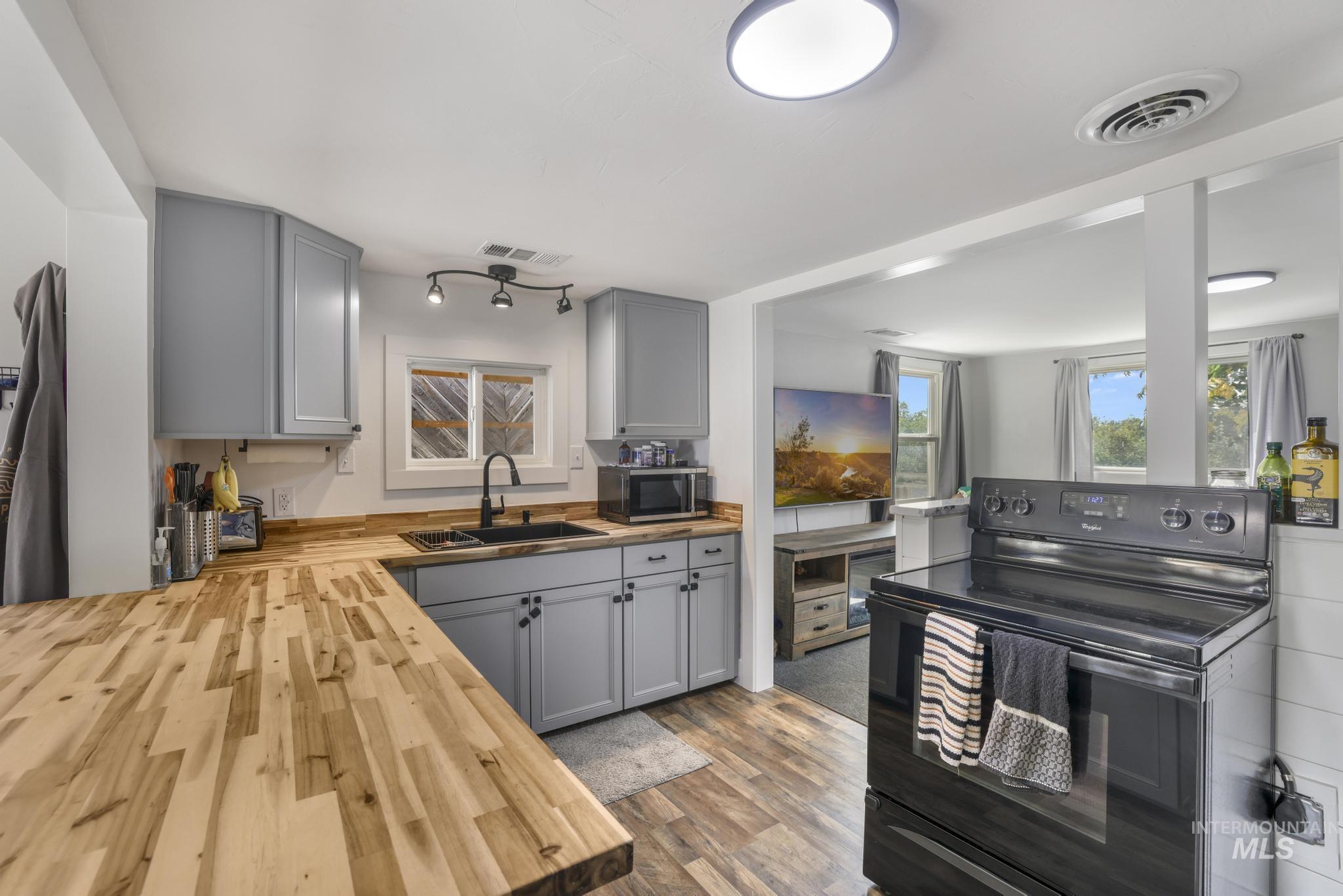 Kitchen featuring gray cabinetry, black range with electric cooktop, wooden counters, and dark wood-style floors