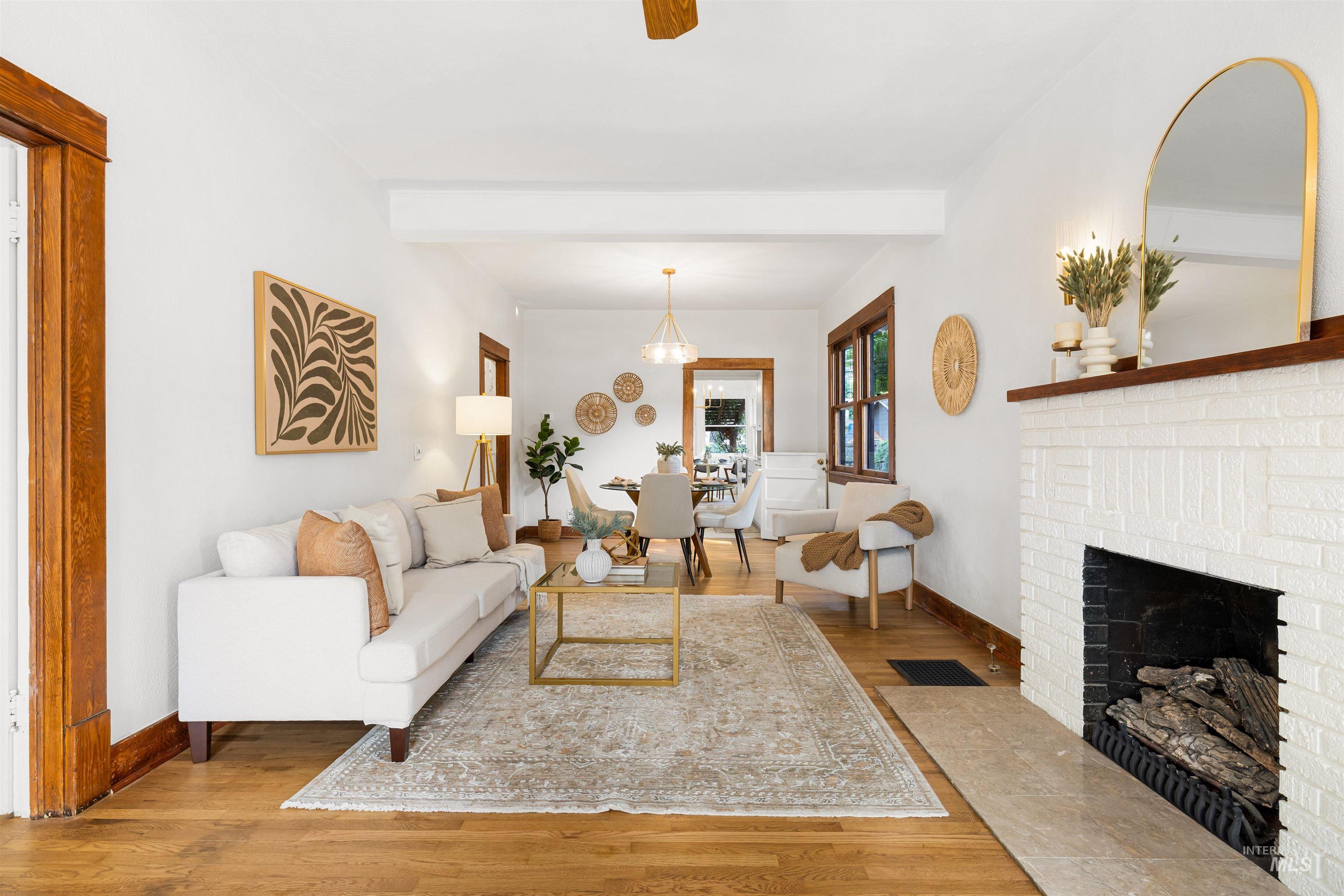 Living room featuring wood finished floors, beam ceiling, a ceiling fan, and a brick fireplace