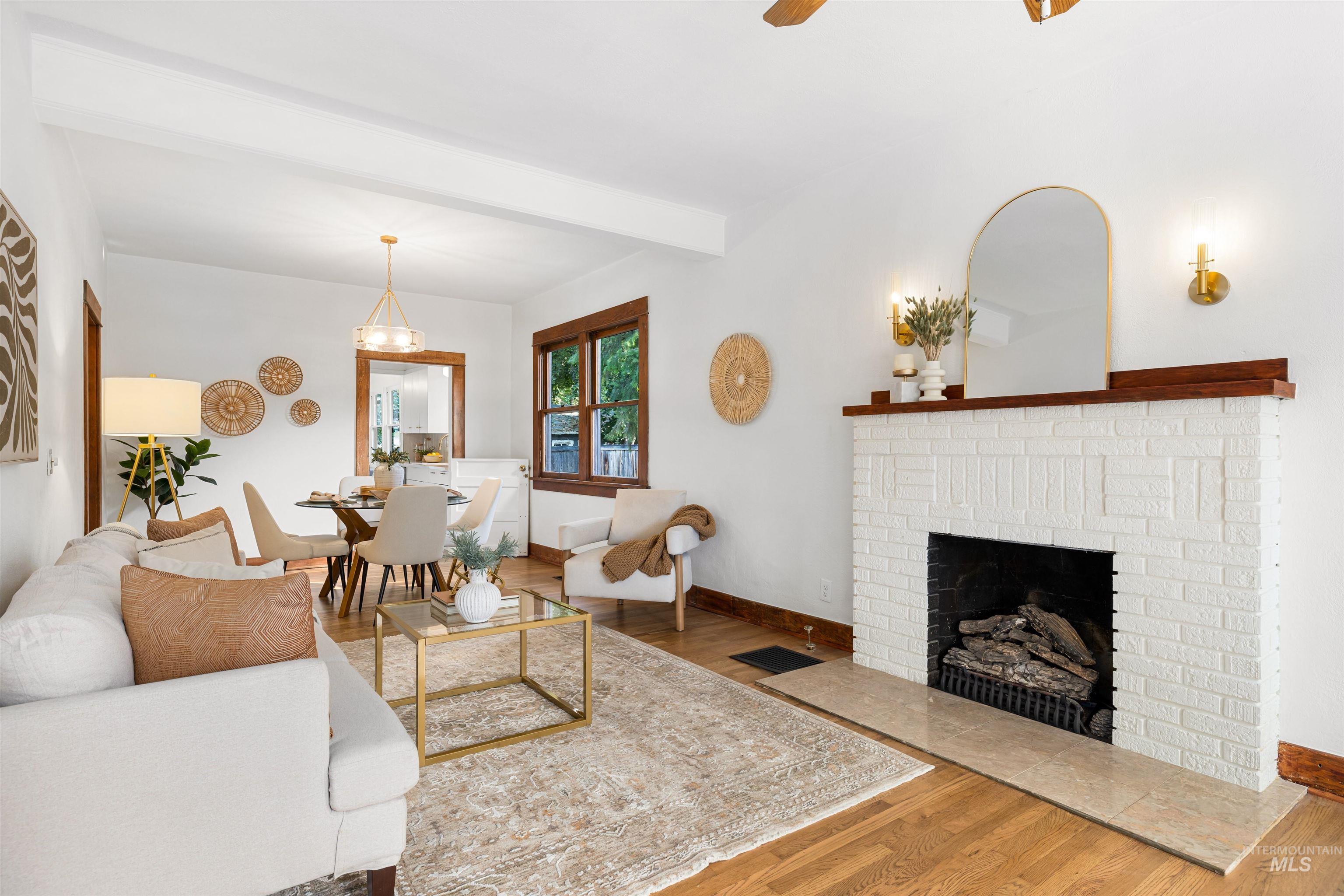 Living room featuring wood finished floors, beam ceiling, a fireplace, and a ceiling fan