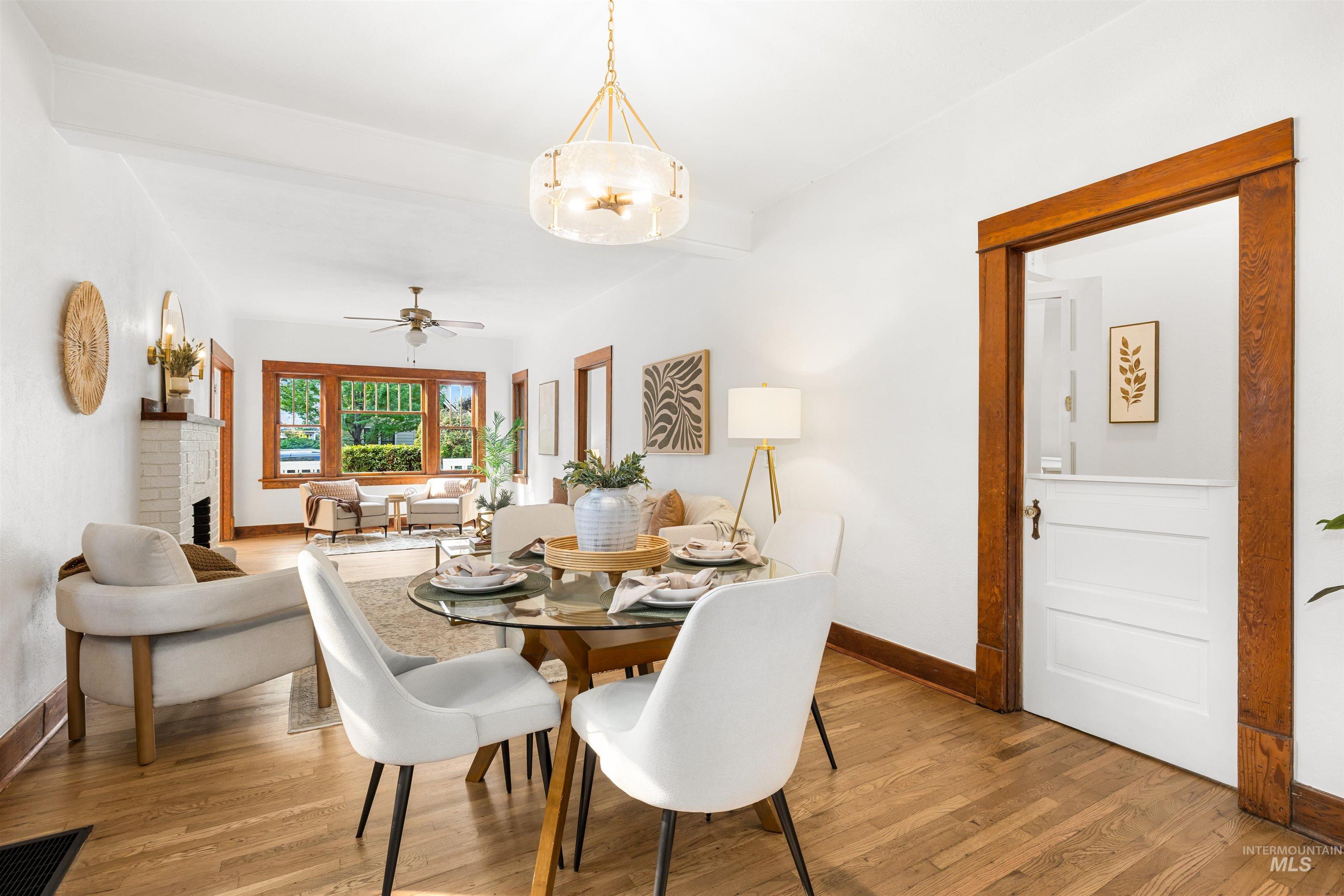 Dining space featuring light wood-type flooring, beamed ceiling, ceiling fan, and a fireplace
