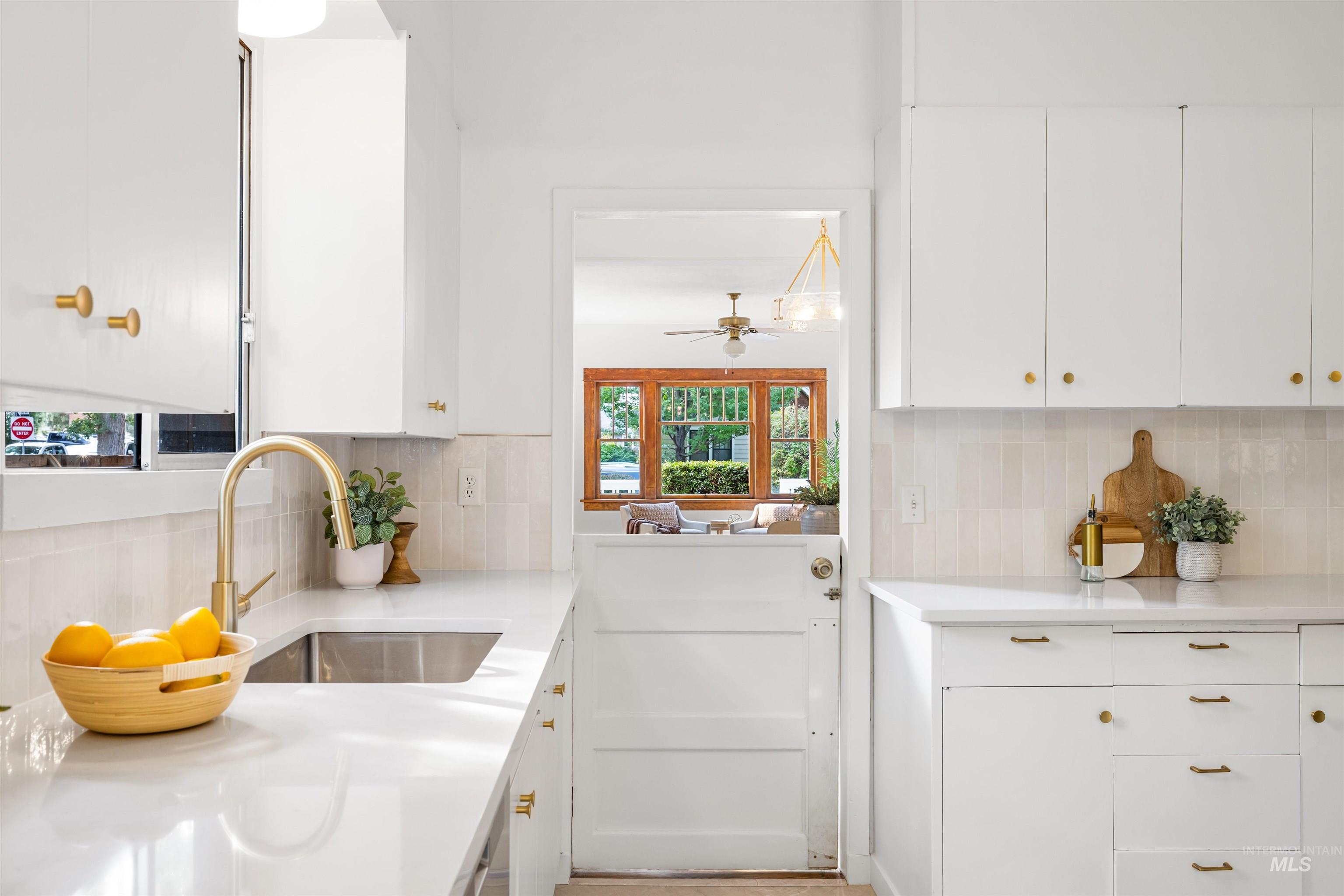 Kitchen with white cabinetry, tasteful backsplash, light stone countertops, and a ceiling fan