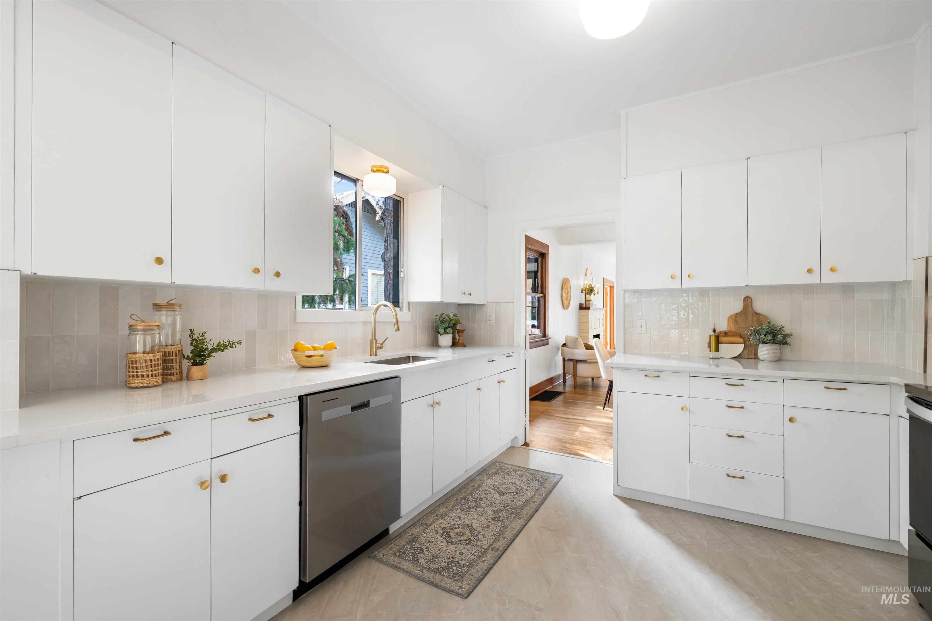 Kitchen featuring white cabinetry, tasteful backsplash, dishwasher, and light stone counters