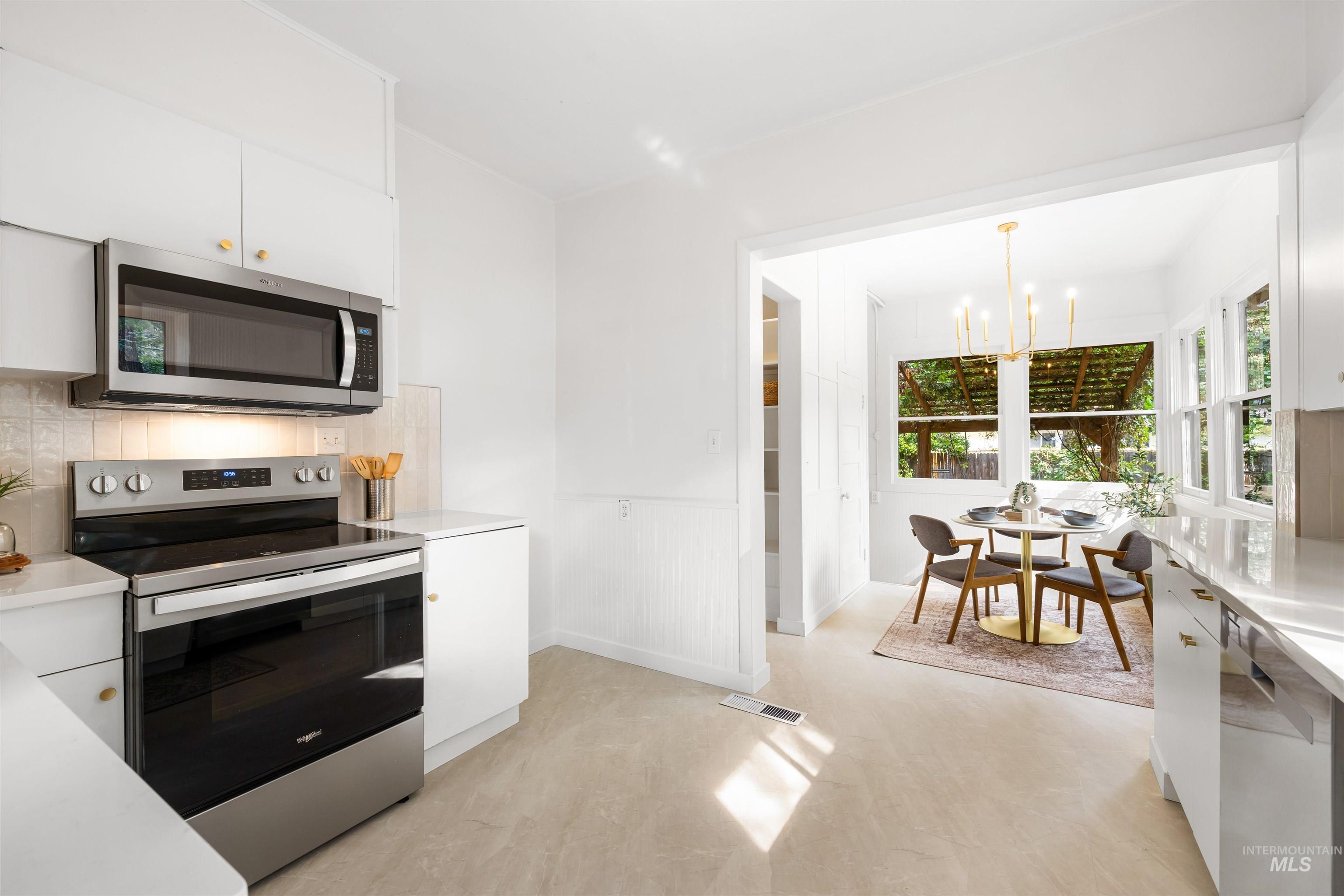 Kitchen with stainless steel appliances, white cabinetry, a chandelier, and decorative light fixtures