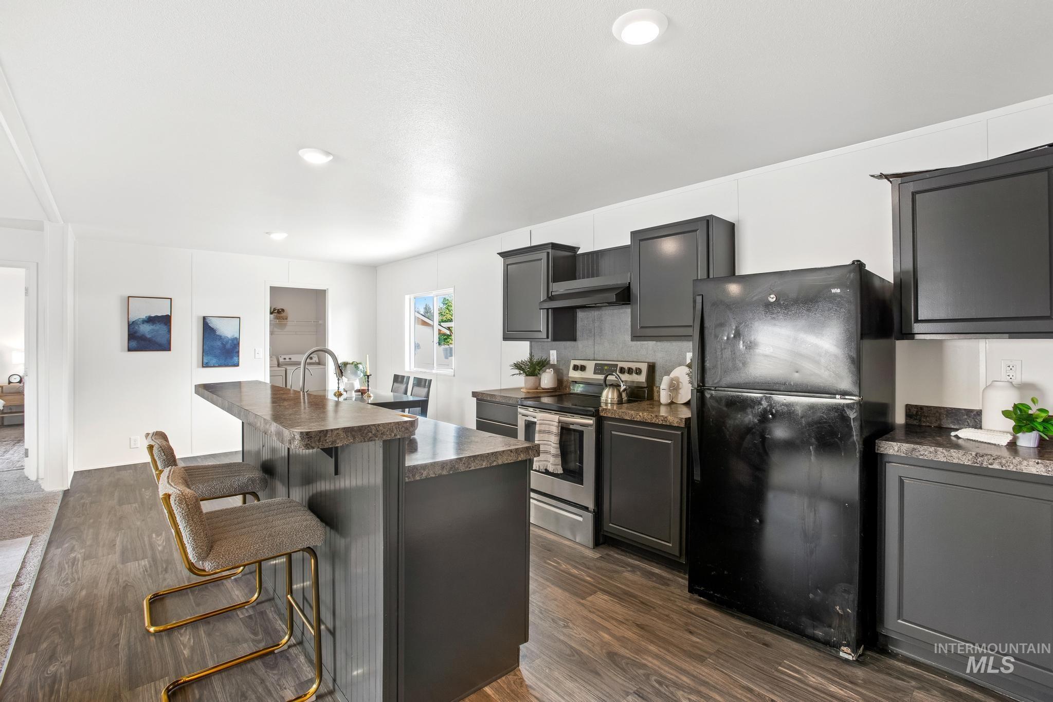 Kitchen featuring a breakfast bar area, freestanding refrigerator, stainless steel electric range, dark countertops, and dark wood finished floors