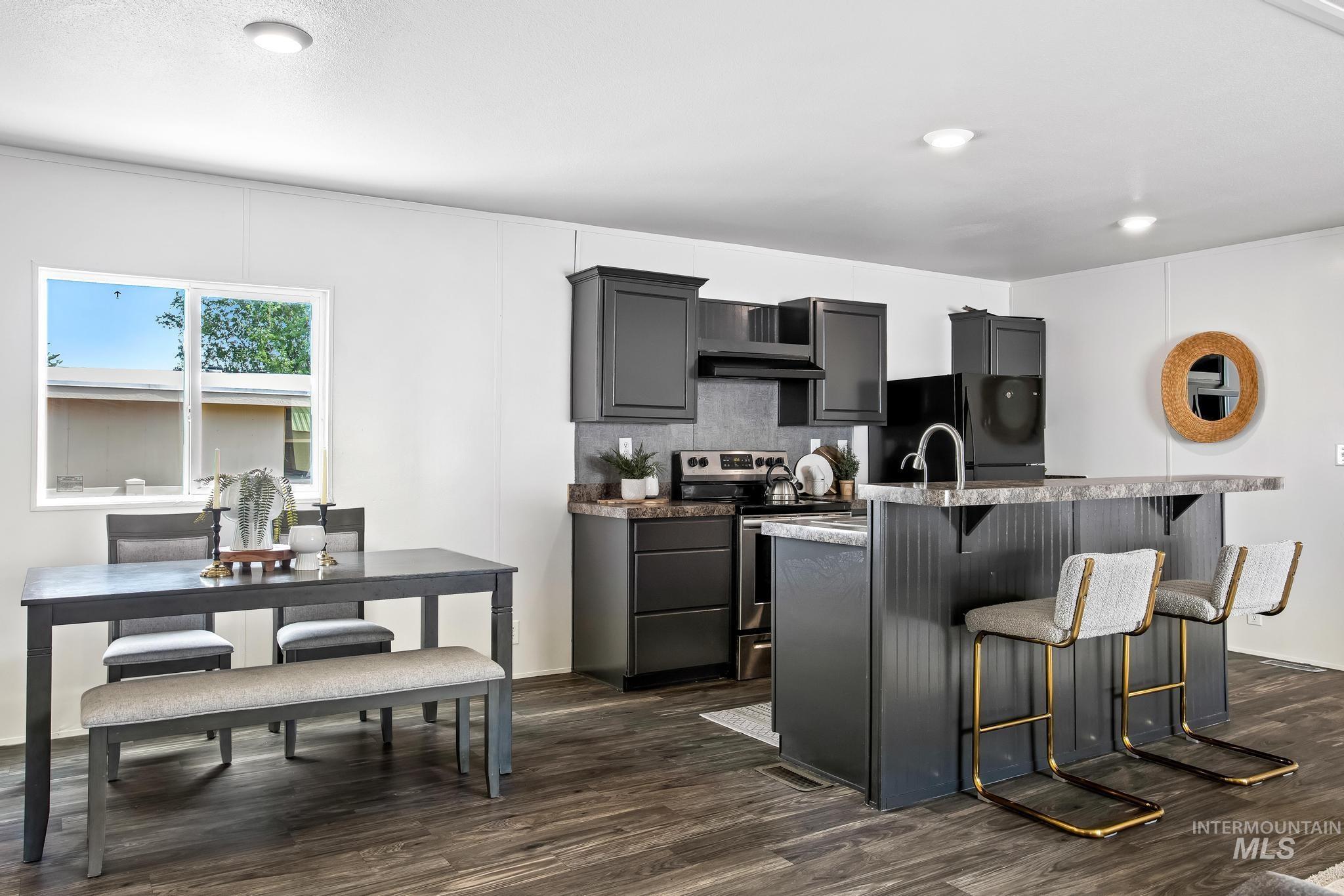 Kitchen featuring a kitchen bar, stainless steel electric range oven, dark wood-type flooring, and freestanding refrigerator