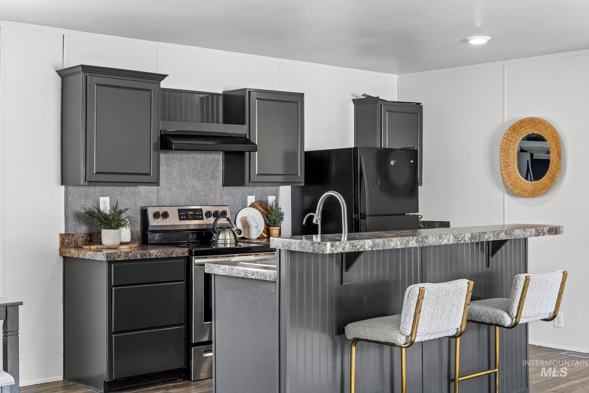 Kitchen featuring stainless steel range with electric cooktop, backsplash, gray cabinets, dark wood finished floors, and freestanding refrigerator