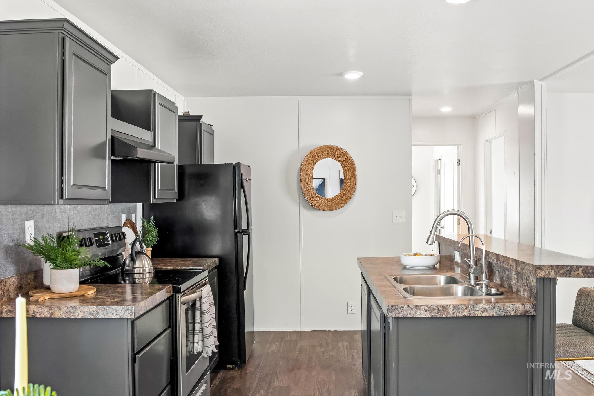 Kitchen with gray cabinetry, stainless steel range with electric stovetop, dark wood-type flooring, a kitchen island with sink, and backsplash
