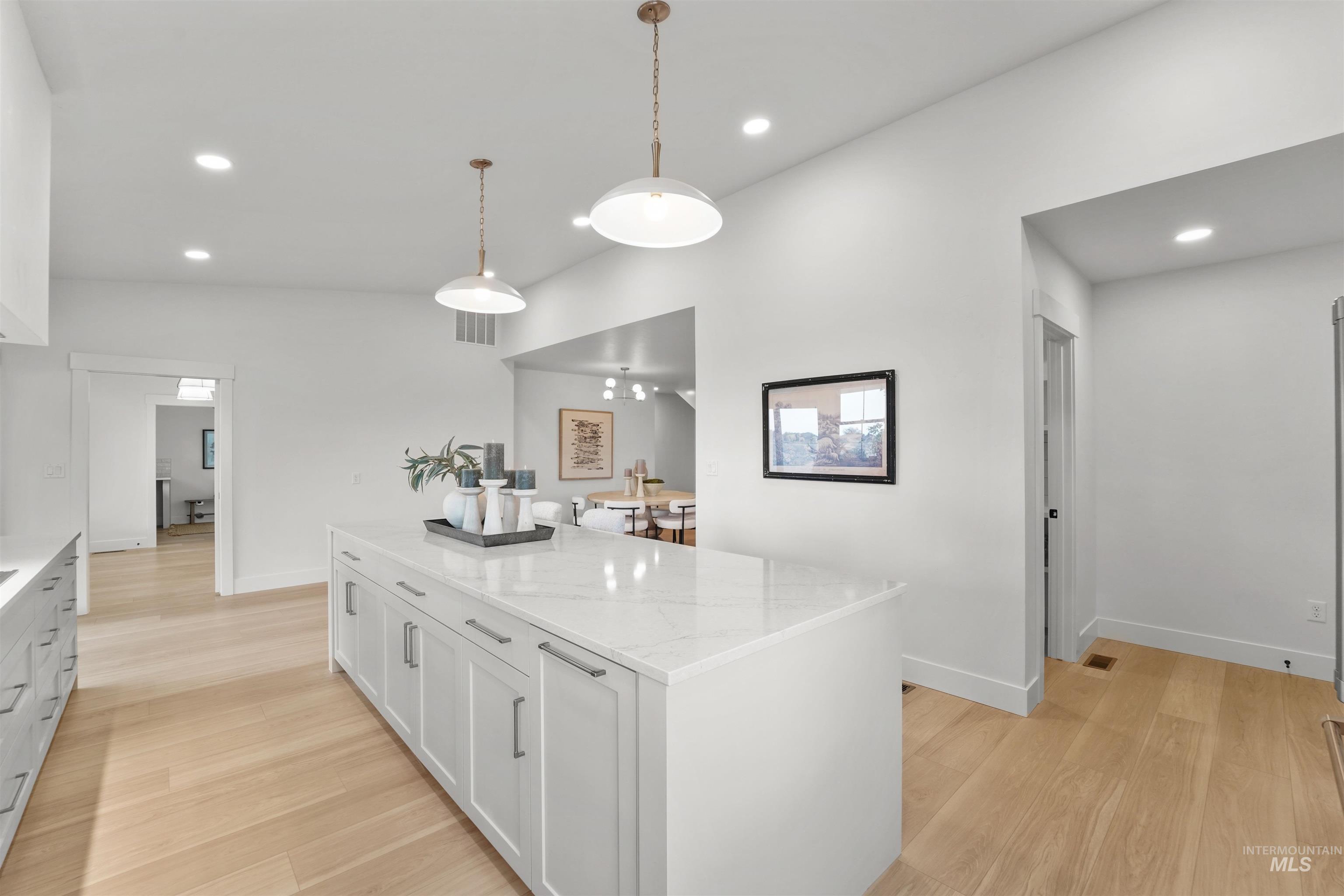 Kitchen with a center island, decorative light fixtures, light stone countertops, recessed lighting, and white cabinetry