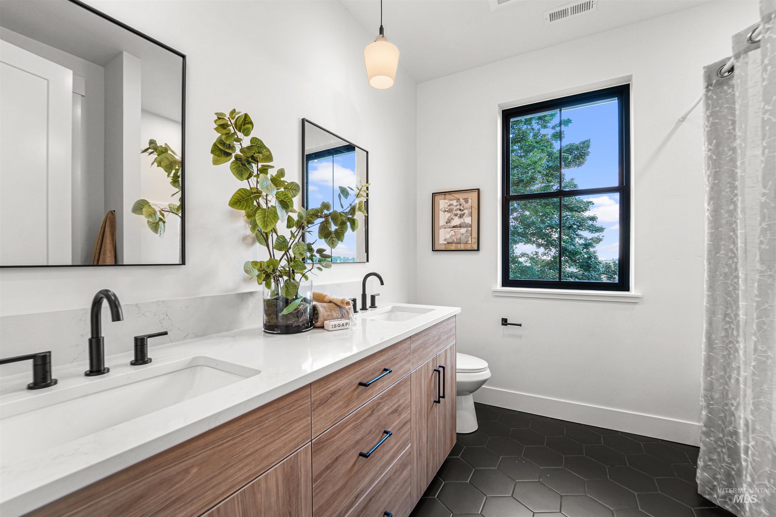 Full bathroom with dark tile patterned floors, double vanity, and curtained shower