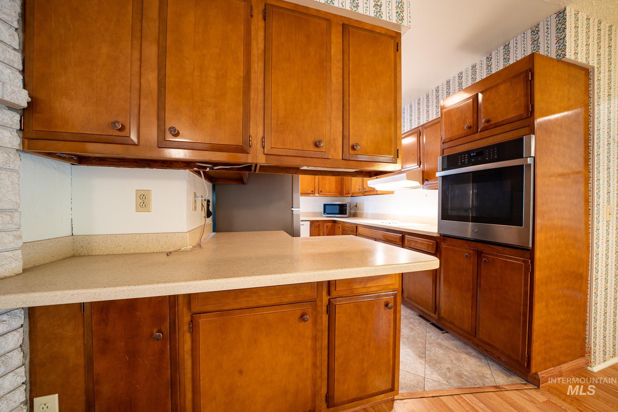 Kitchen with appliances with stainless steel finishes, brown cabinets, light countertops, a peninsula, and light wood-type flooring