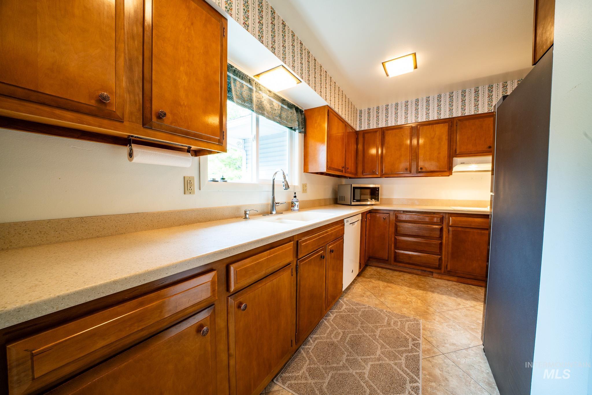 Kitchen with brown cabinetry, appliances with stainless steel finishes, and light tile patterned floors