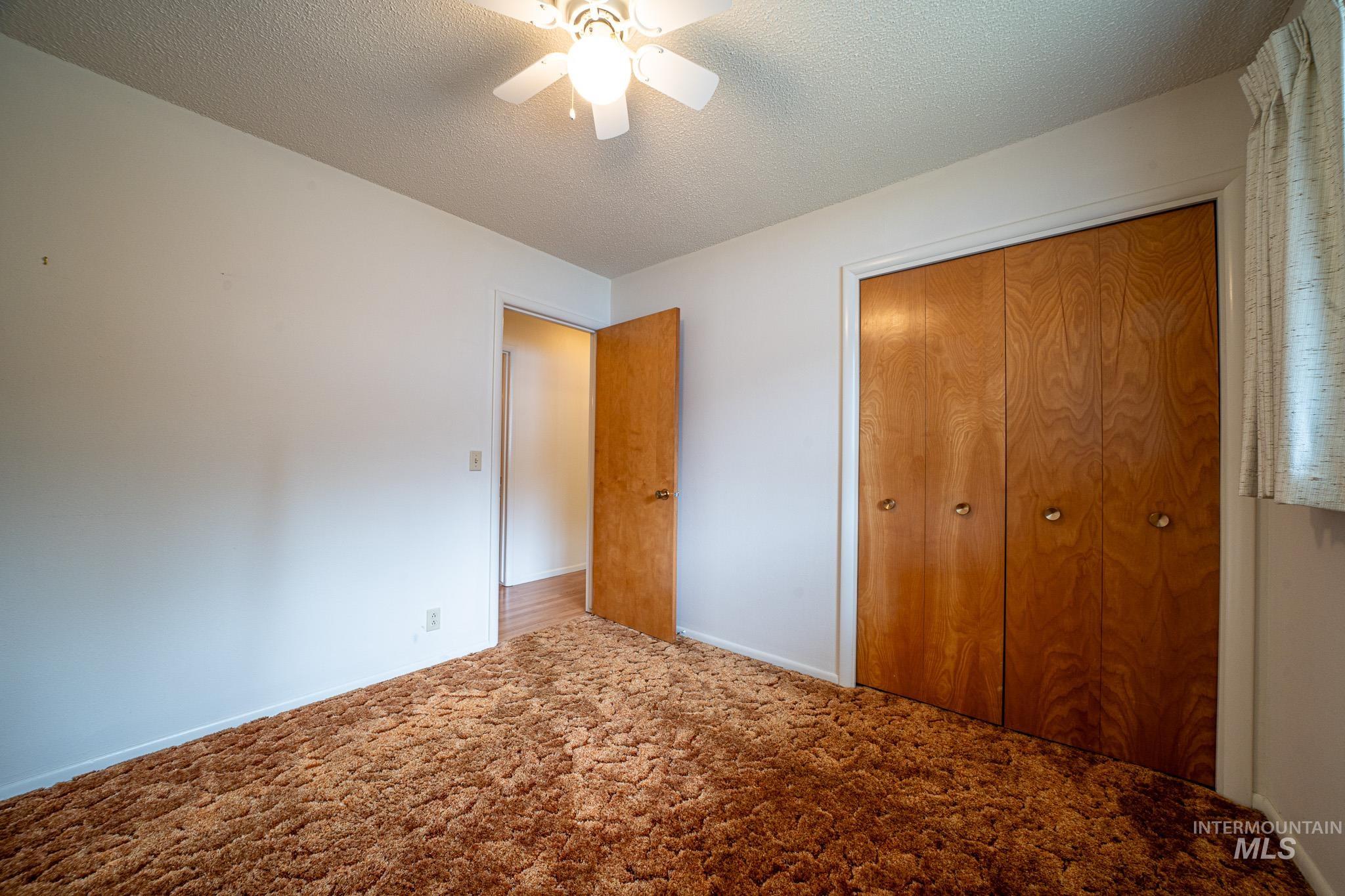 Unfurnished bedroom with a textured ceiling, carpet, a closet, and a ceiling fan