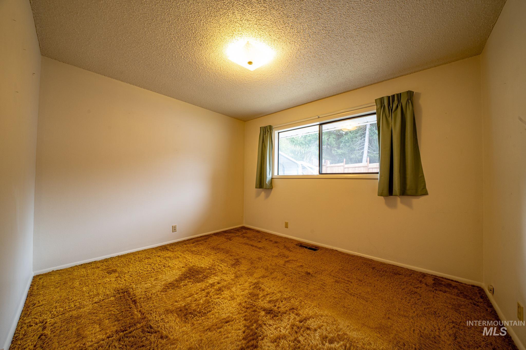 Carpeted spare room with a textured ceiling and baseboards