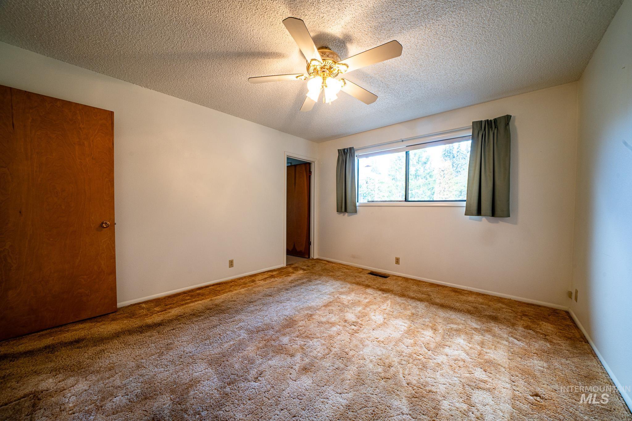 Carpeted spare room with a ceiling fan and a textured ceiling