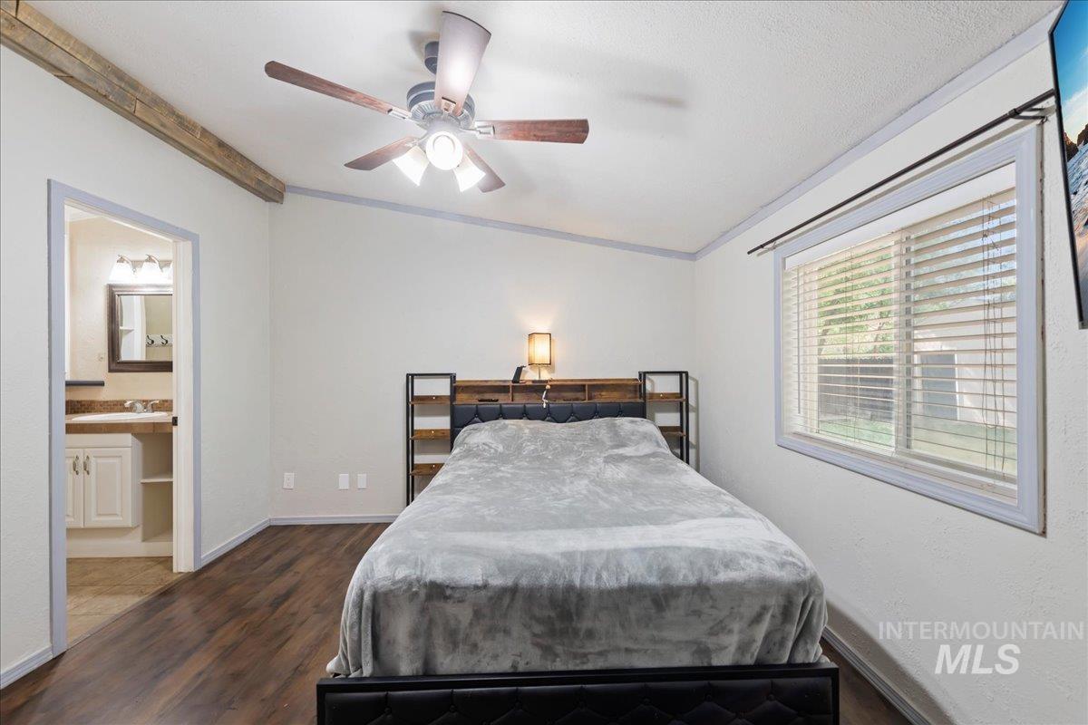 Bedroom featuring ornamental molding, dark wood finished floors, a ceiling fan, and ensuite bath