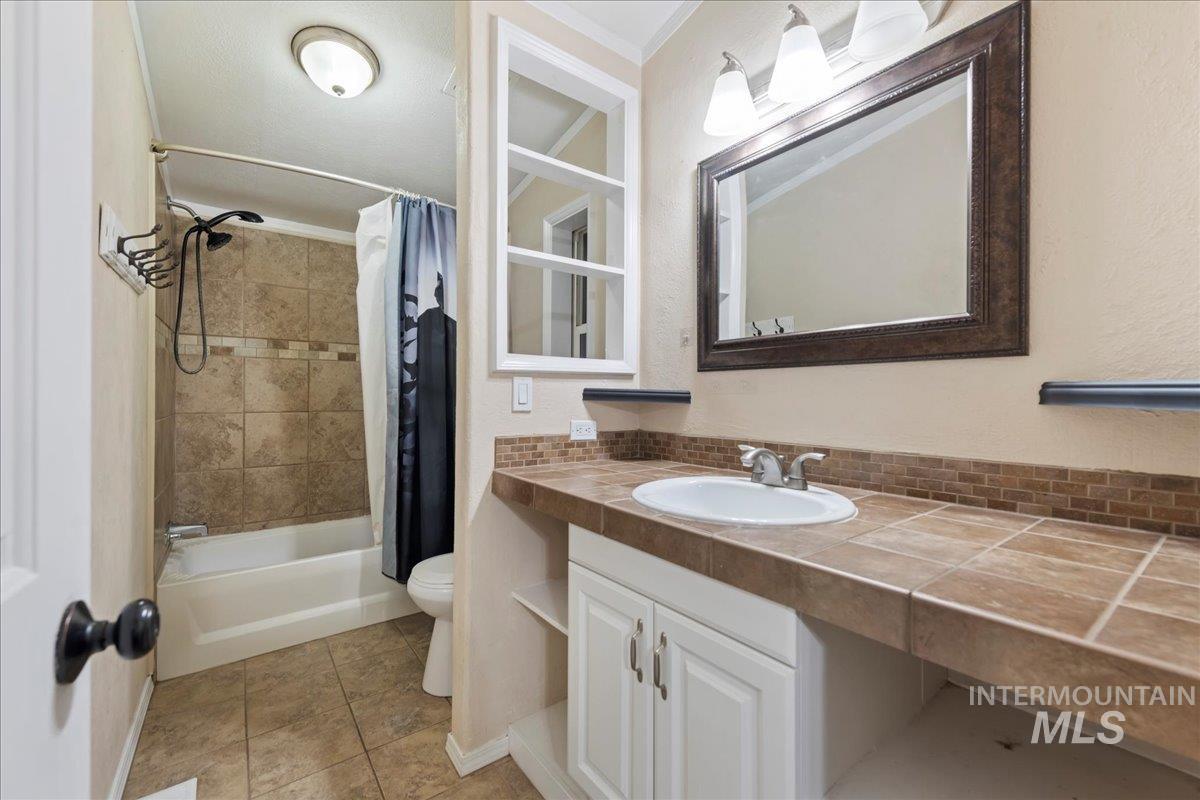 Full bath featuring shower / tub combo with curtain, vanity, light tile patterned floors, and a textured wall
