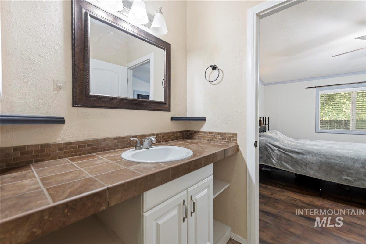 Bathroom featuring a textured wall, vanity, dark wood-style flooring, a ceiling fan, and ensuite bath