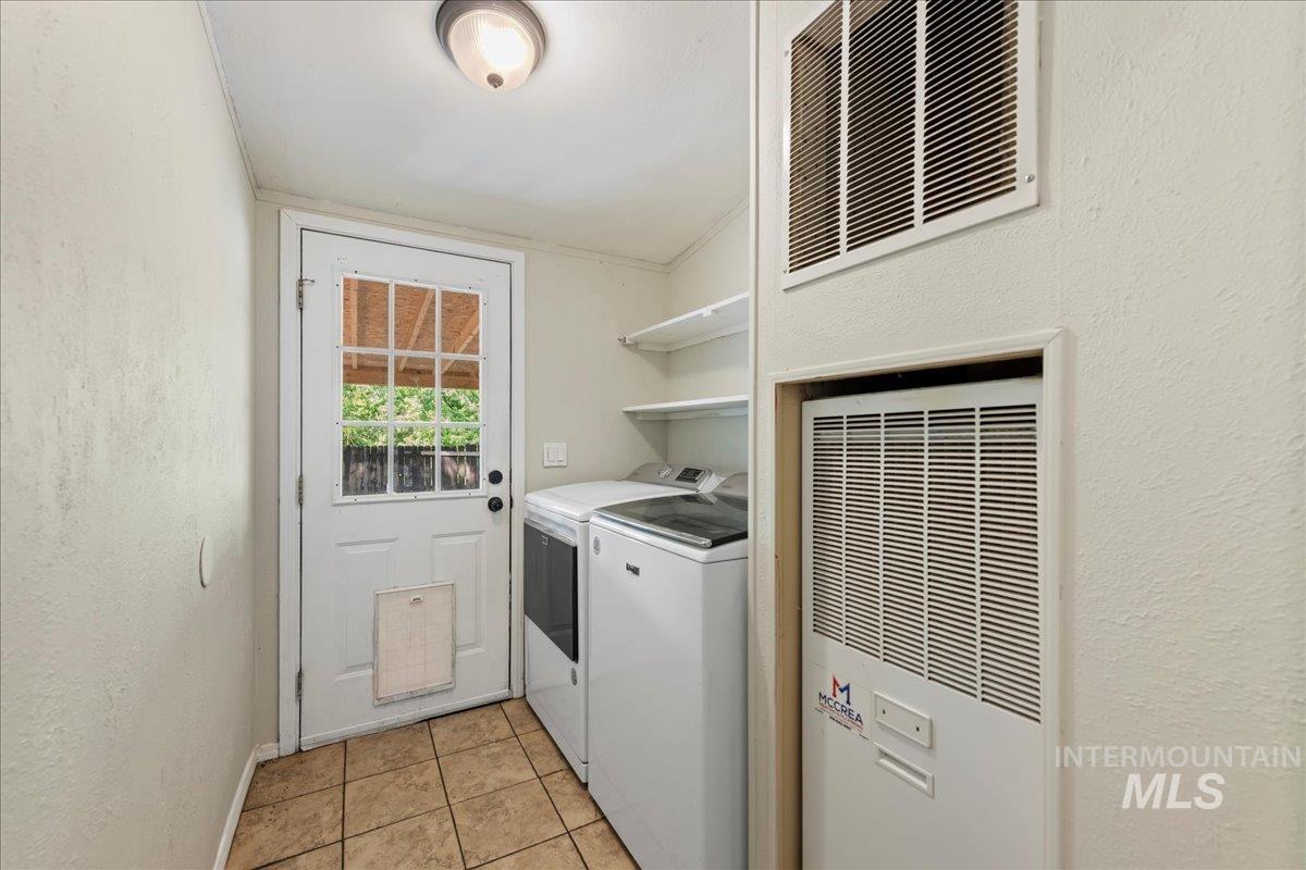 Washroom with a textured wall, a heating unit, washing machine and dryer, and light tile patterned floors