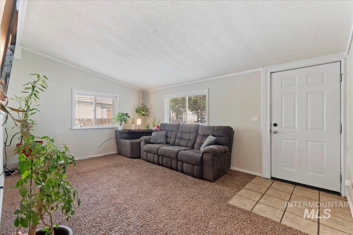 Living room featuring a textured ceiling, light colored carpet, crown molding, lofted ceiling, and light tile patterned floors