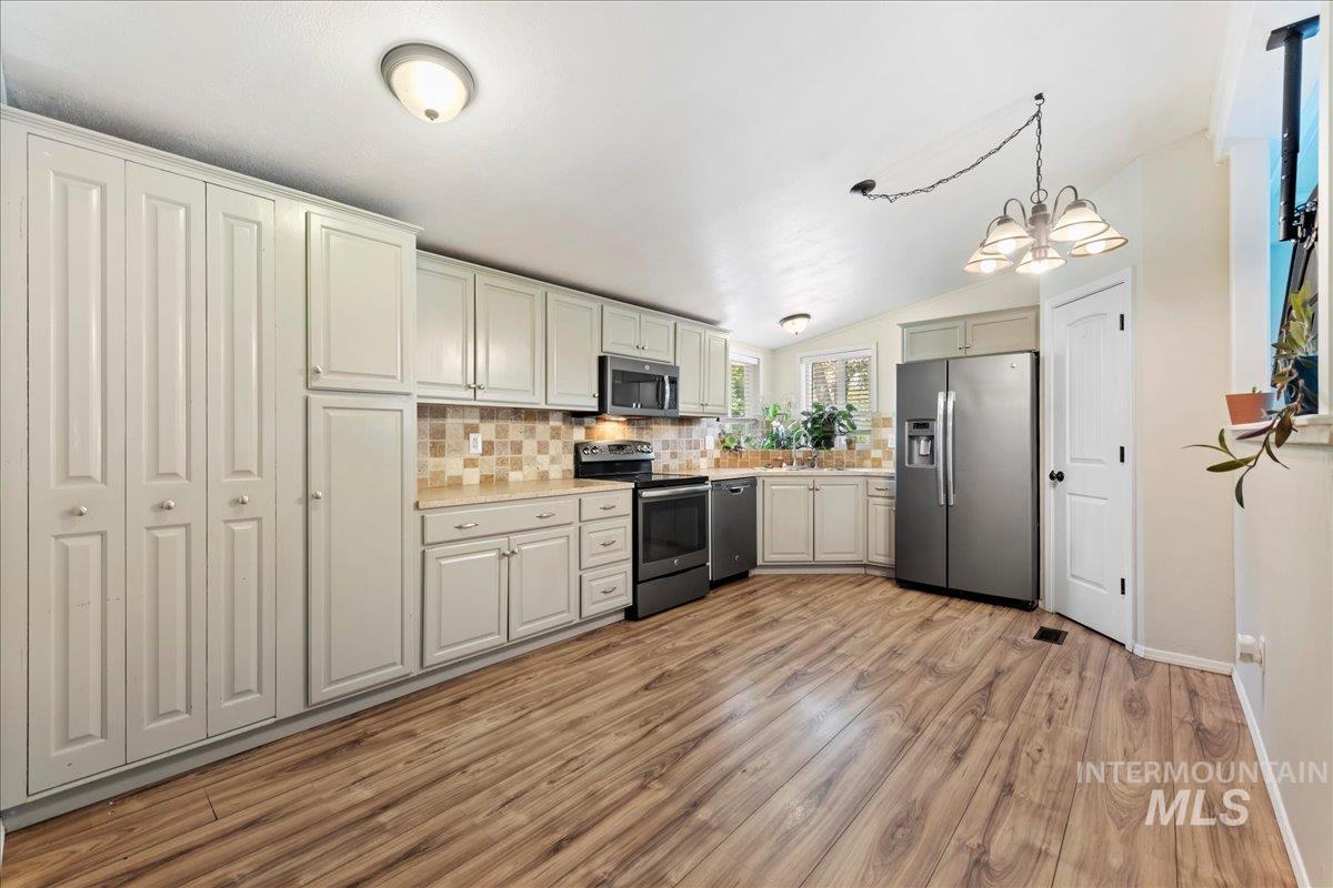 Kitchen featuring vaulted ceiling, decorative backsplash, appliances with stainless steel finishes, light countertops, and light wood-style floors