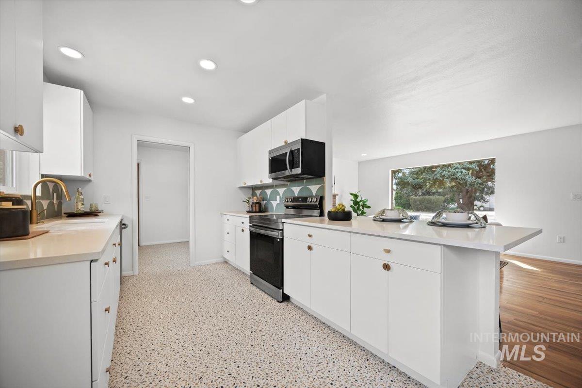 Kitchen with stainless steel appliances, white cabinetry, recessed lighting, a peninsula, and light stone counters