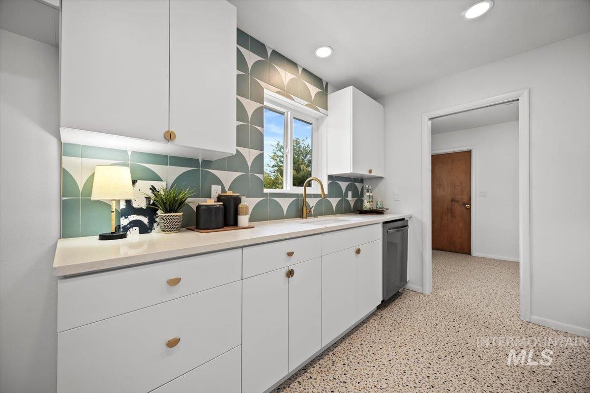 Kitchen with white cabinetry, backsplash, dark aggregate flooring, and recessed lighting