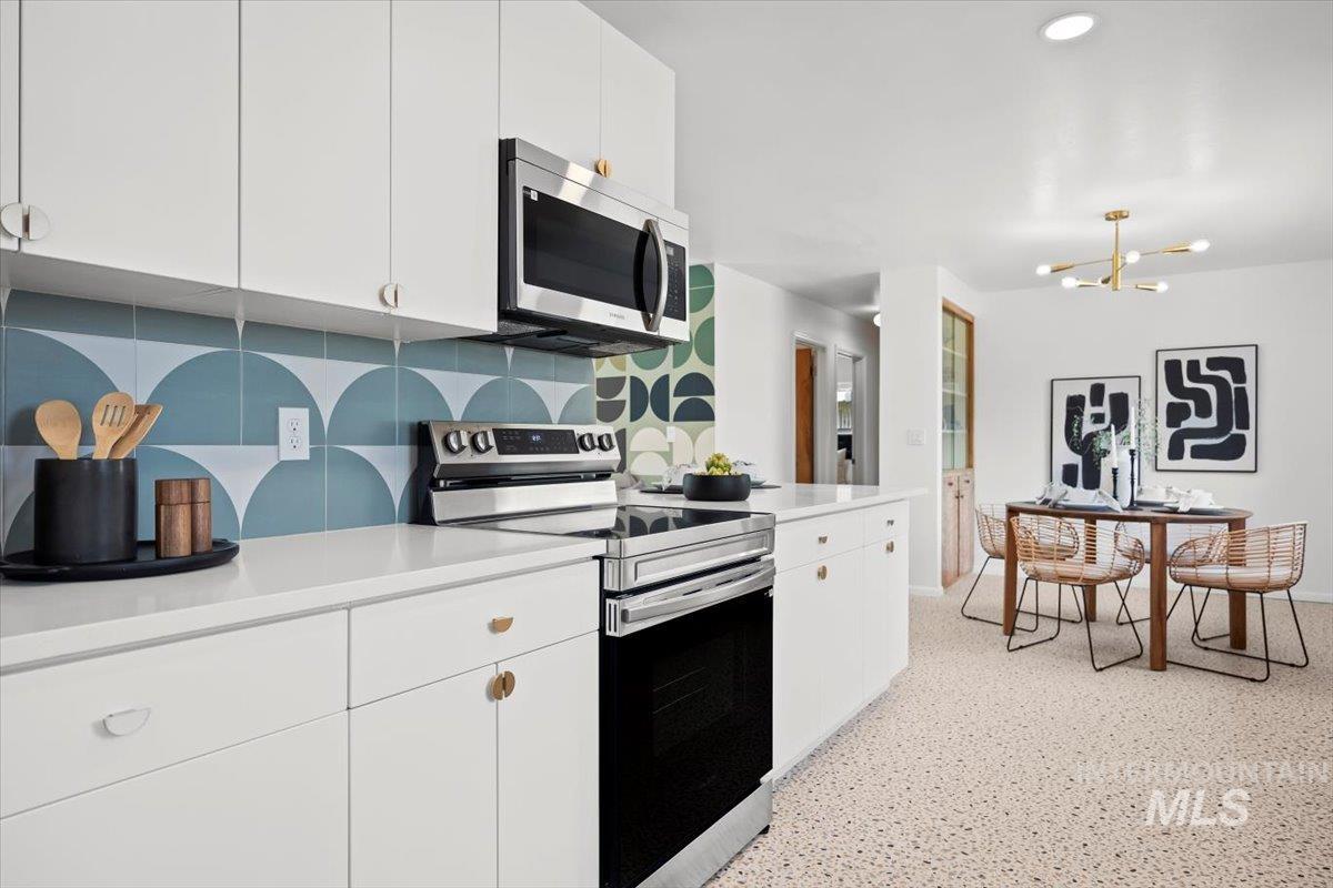 Kitchen featuring appliances with stainless steel finishes, white cabinets, decorative backsplash, dark aggregate flooring, and a chandelier