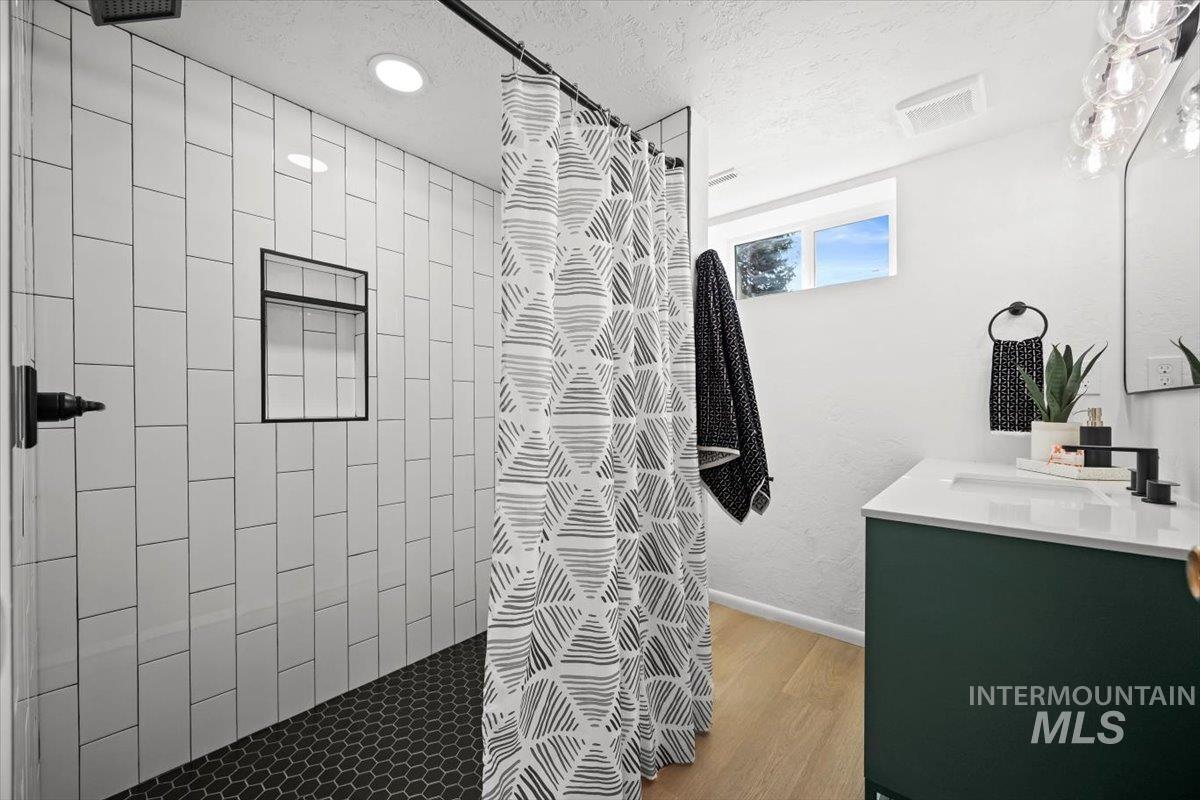 Full bath with tiled shower, vanity, a textured ceiling, and light wood-style flooring