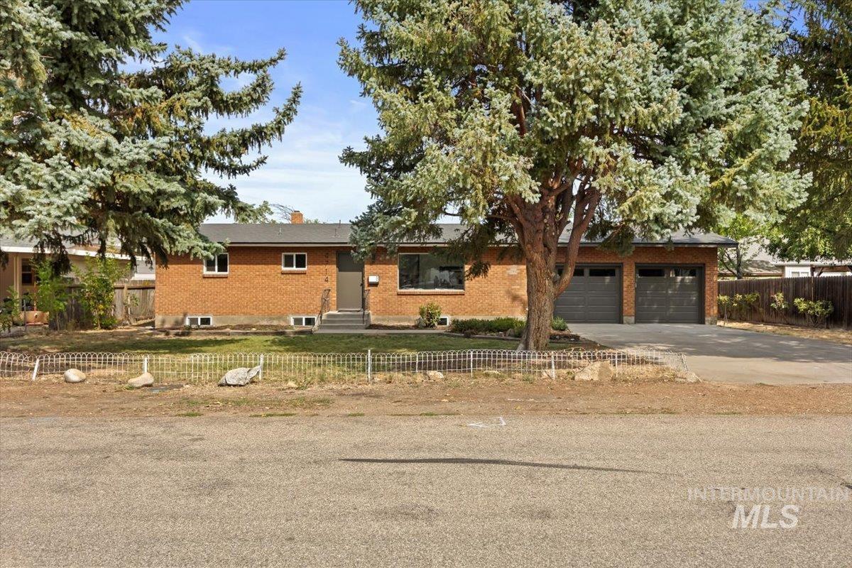 Ranch-style home with a fenced front yard, concrete driveway, a chimney, brick siding, and entry steps